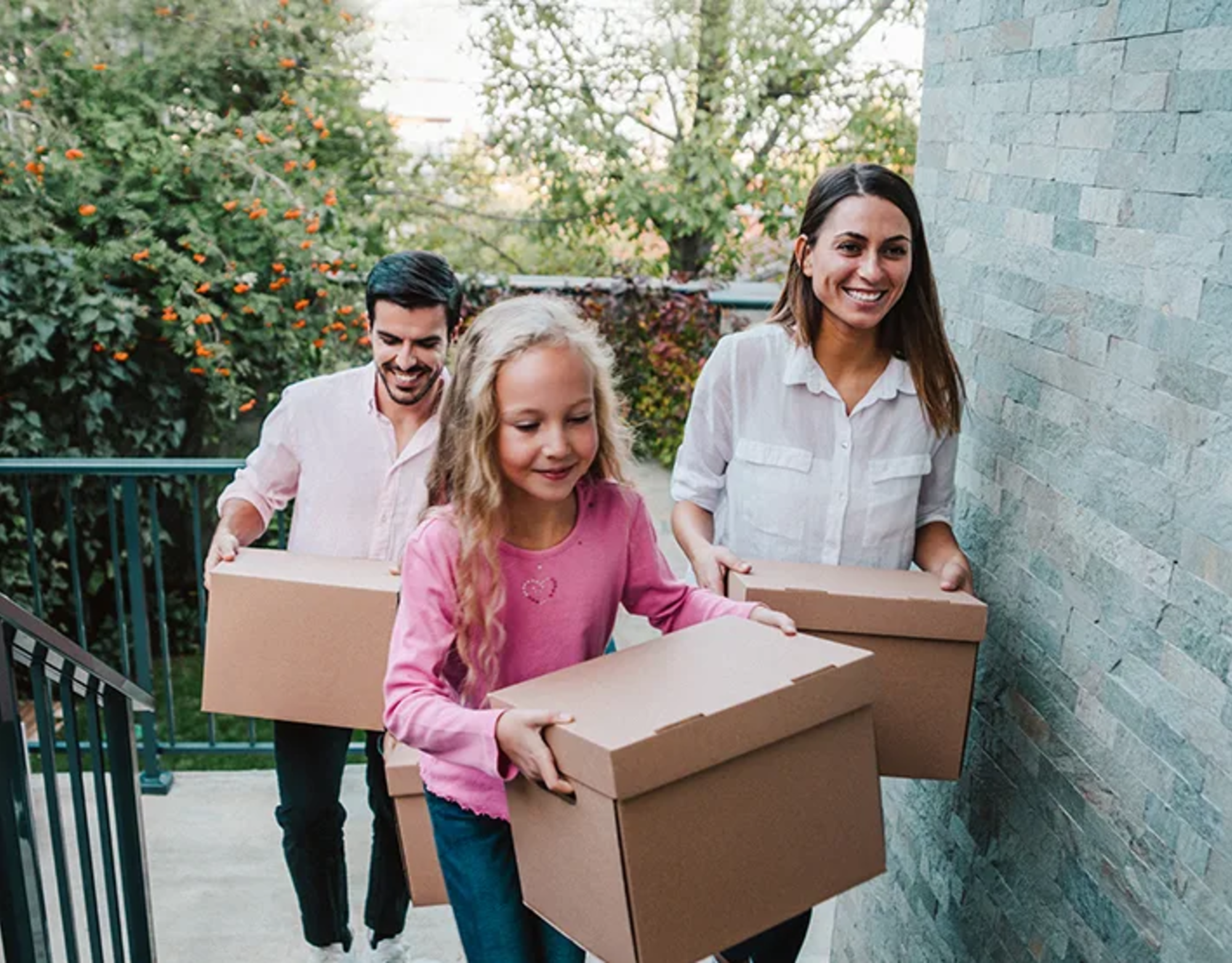 Smiling couple and child carry cardboard boxes while moving into a new home together.