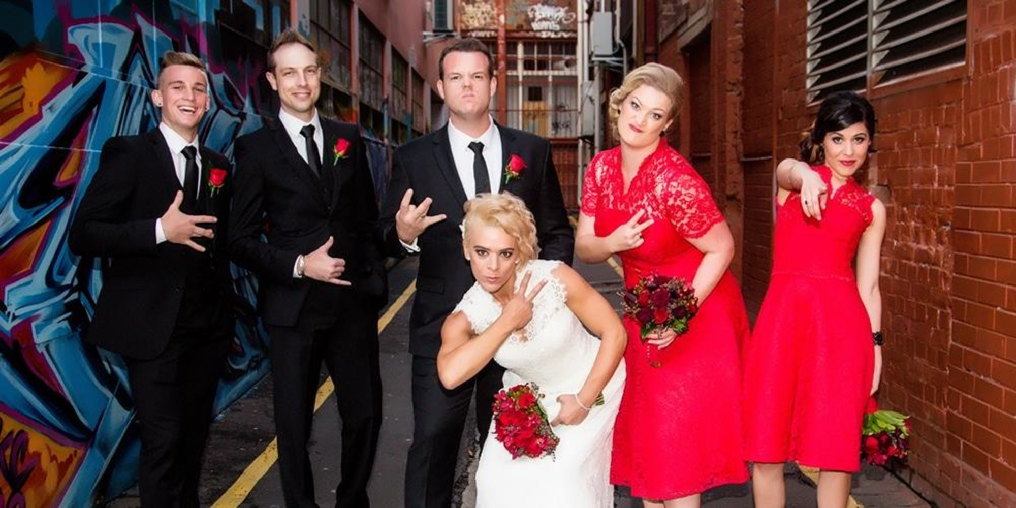 Wedding party posing playfully in an urban alley with red accents and graffiti walls.