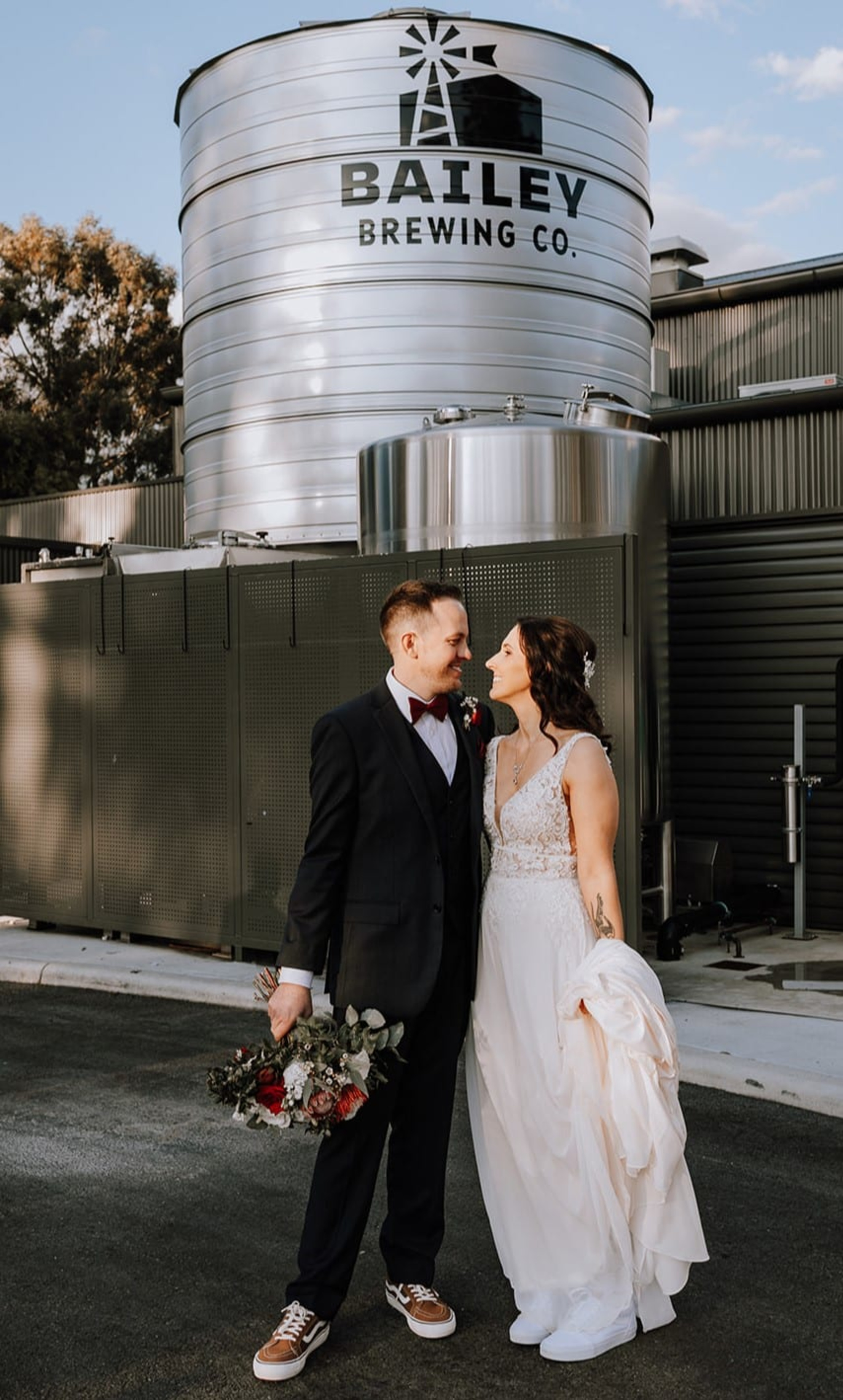 Bride and groom share a moment in front of the Bailey Brewing Co. tanks at an industrial brewery wedding venue.
