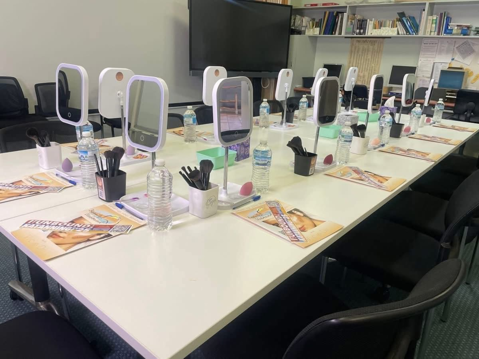 Classroom-style table set with mirrors, makeup brushes, and water bottles for a bridal makeup workshop.