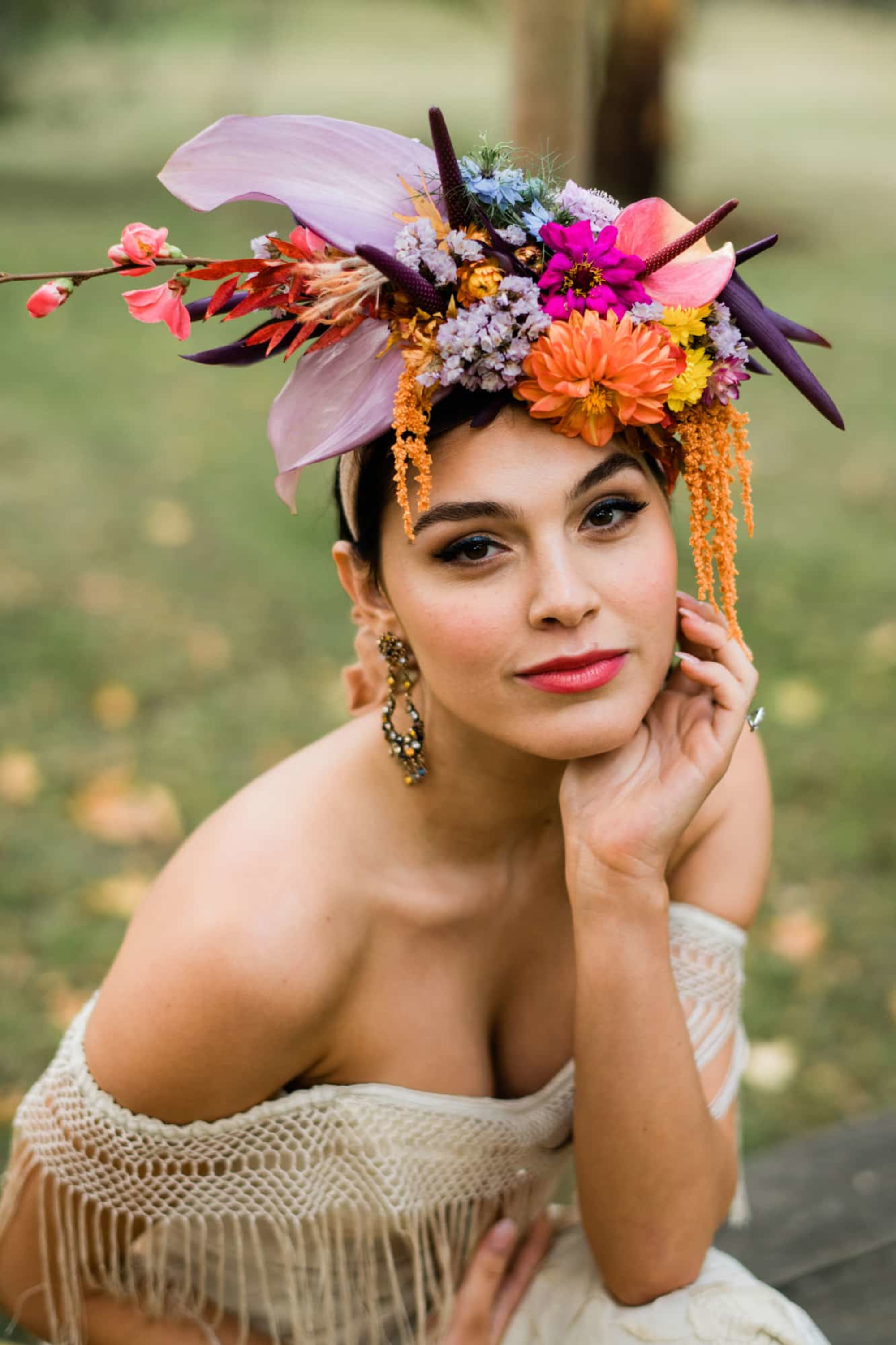 Boho bride posing outdoors wearing a vibrant, oversized floral headpiece and off-the-shoulder gown.