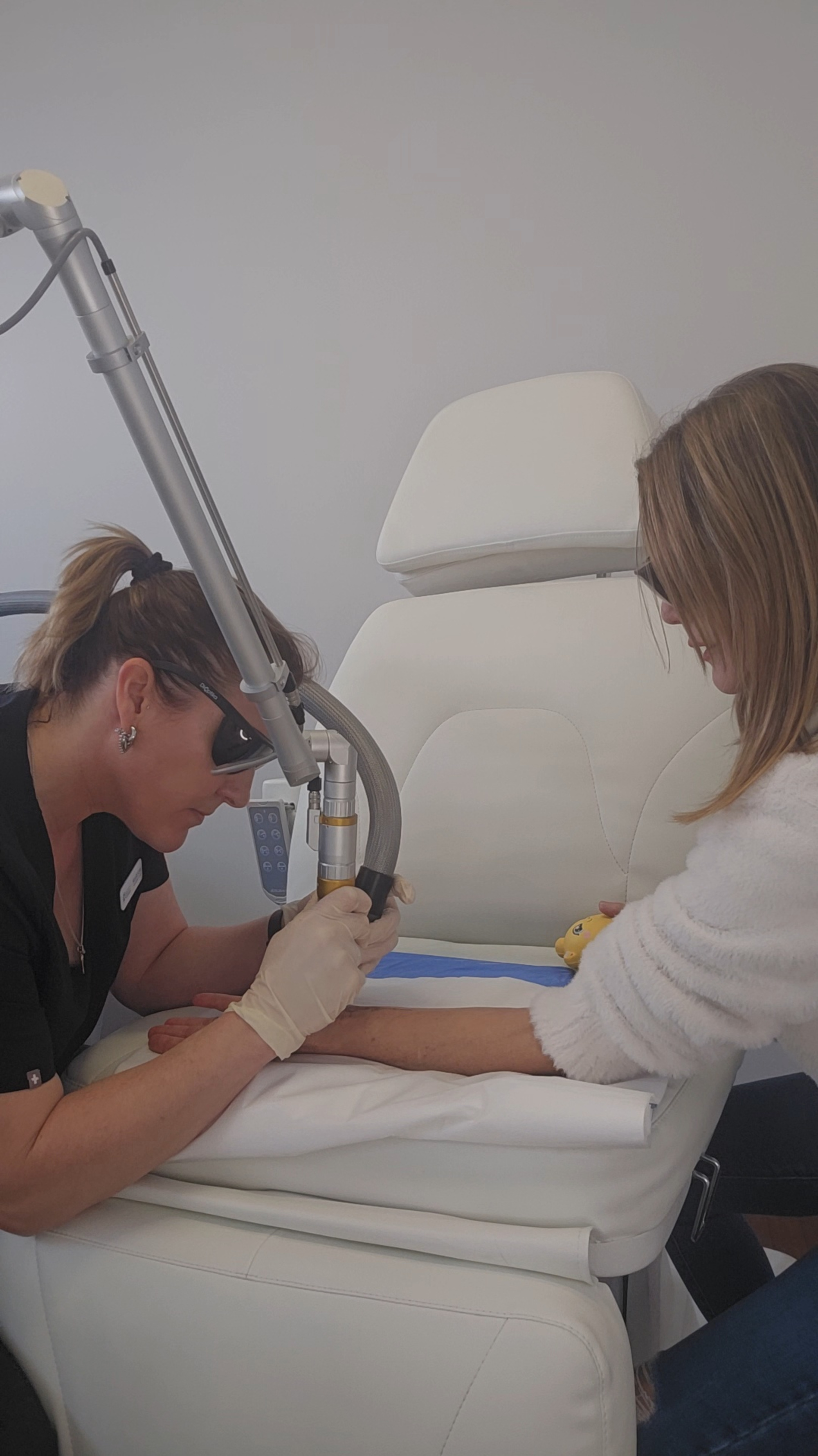 Technician performs a laser skincare treatment on a woman in a modern clinic chair.