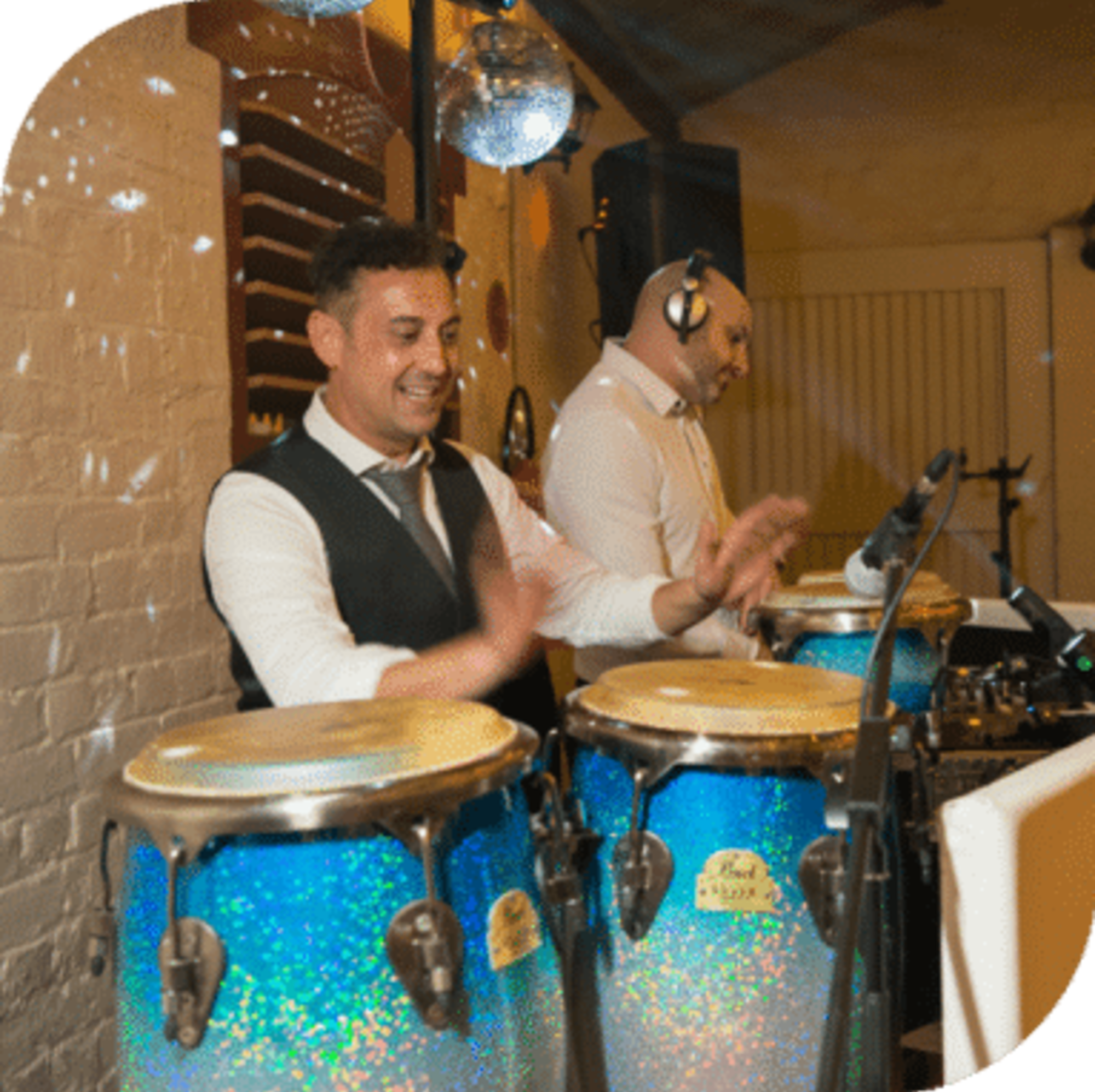 Percussionist and DJ performing lively music with blue conga drums at an indoor wedding reception.