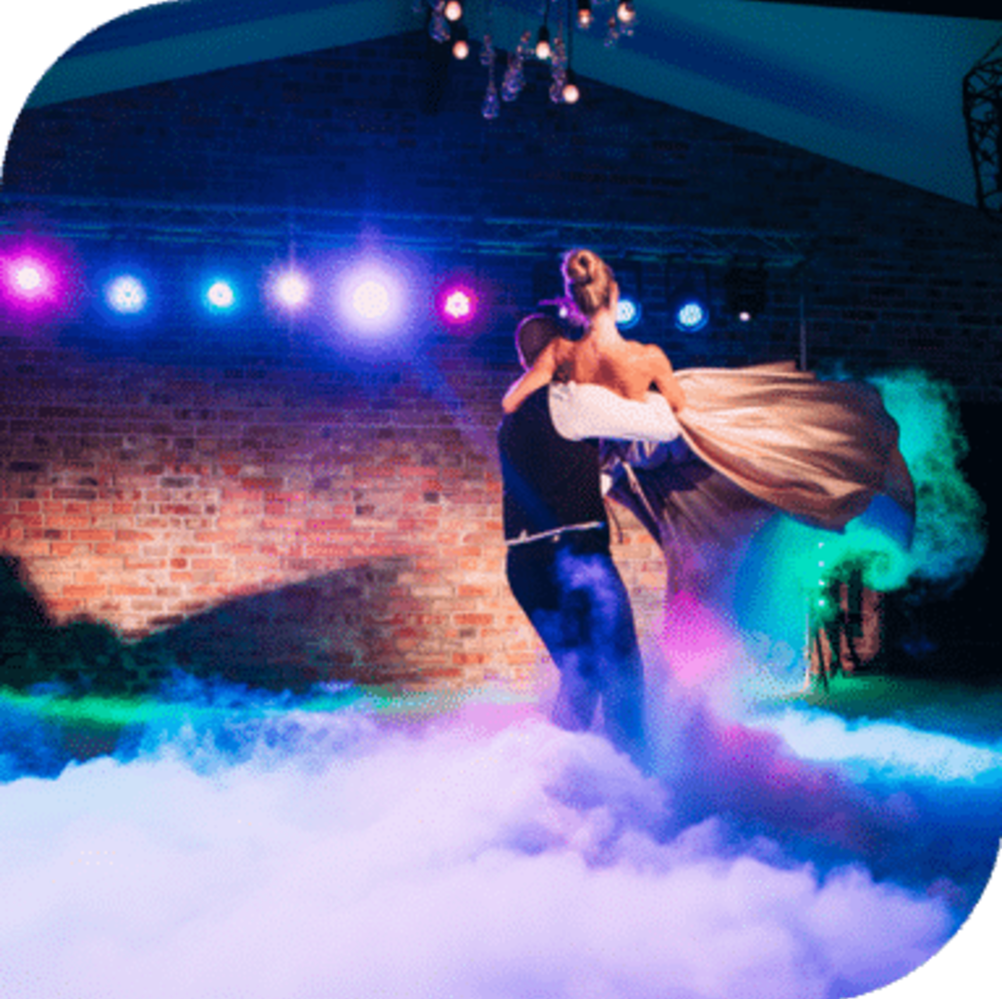 Bride and groom share a dramatic first dance on a fog-filled, colorfully lit wedding dance floor.