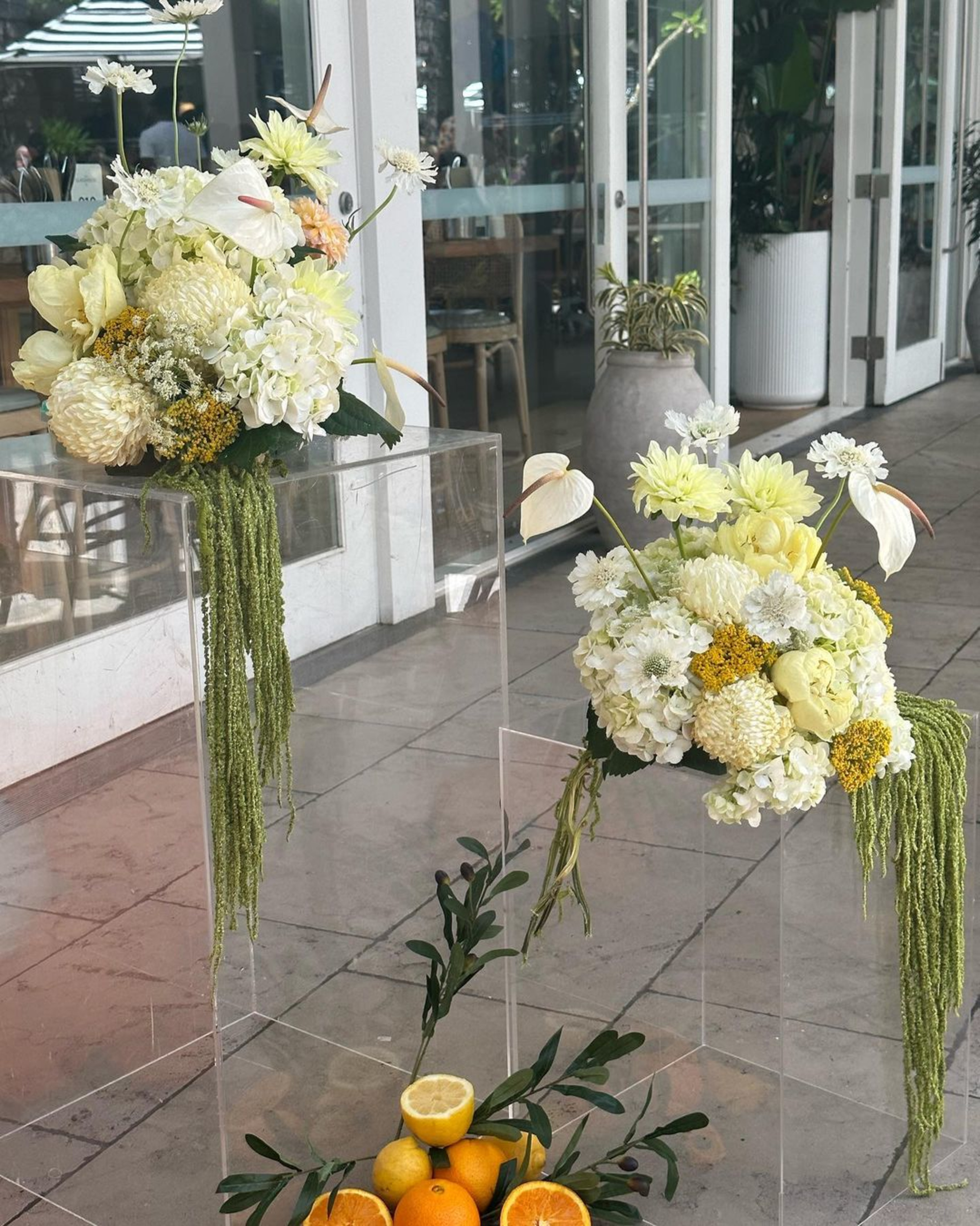 Modern wedding floral arrangements with white and yellow blooms and citrus accents displayed on clear stands.