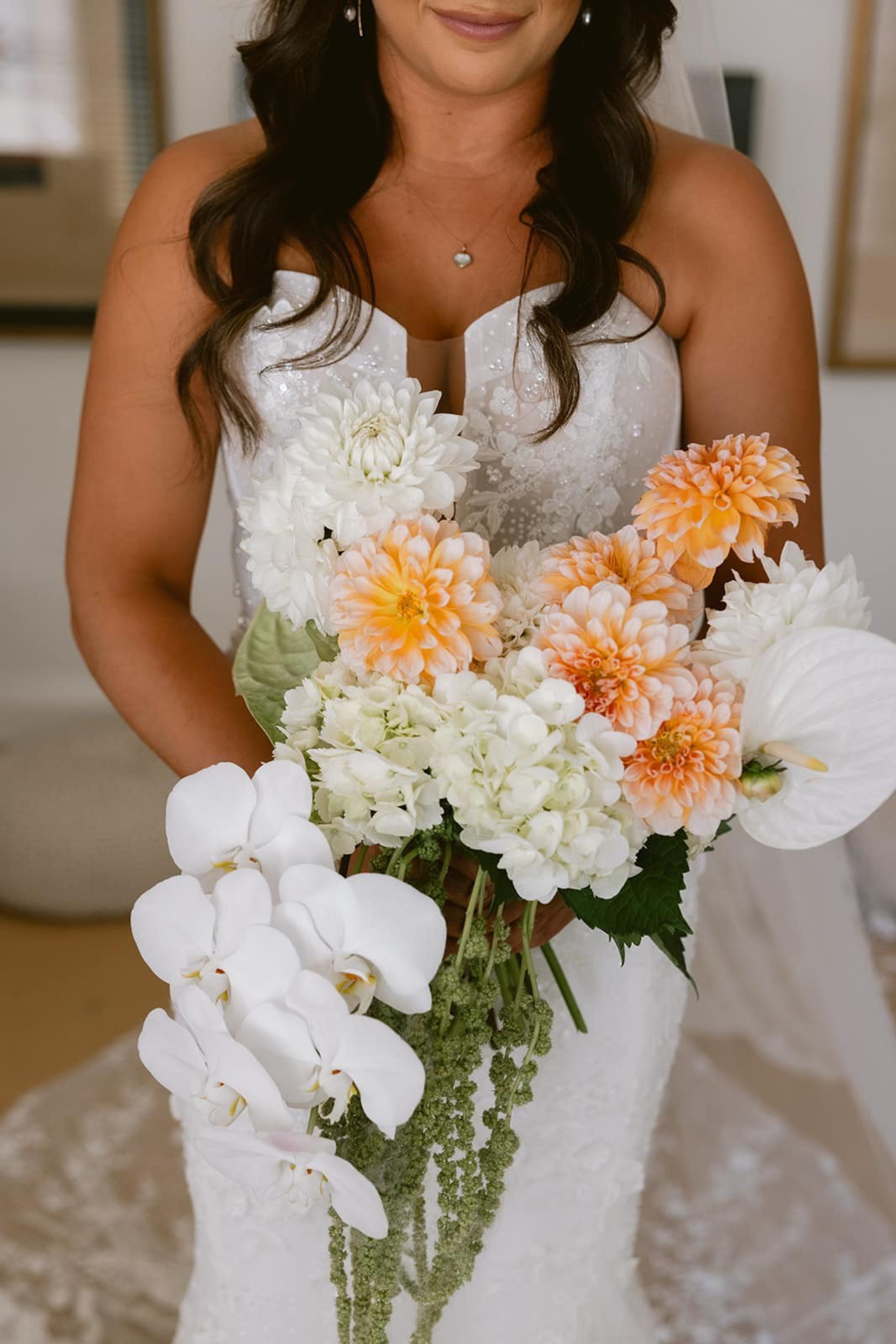 Bride in a white gown holding a cascading bouquet of white orchids and peach and white flowers.