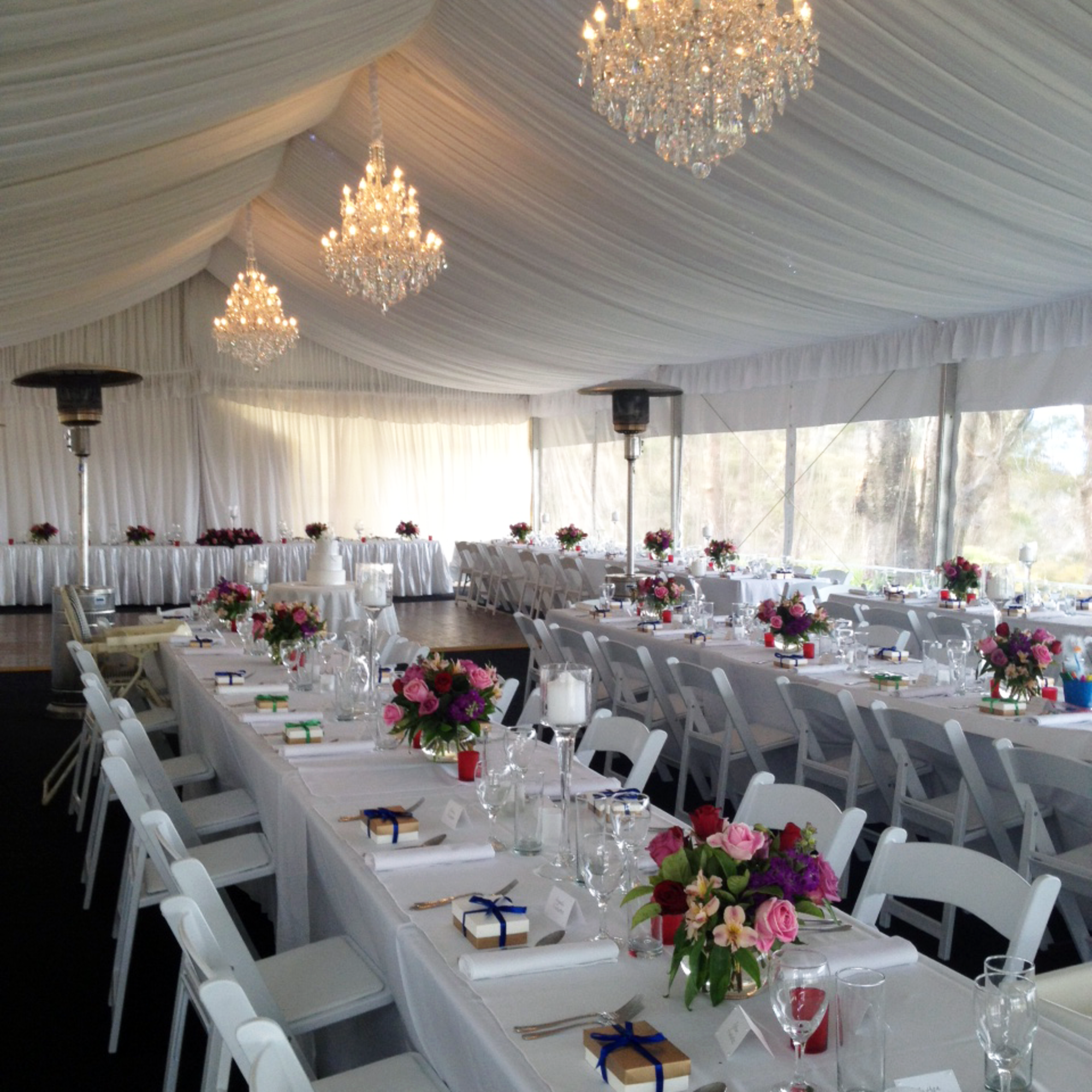 Elegant wedding reception in a draped marquee with chandeliers, white tables, and colorful floral centerpieces.