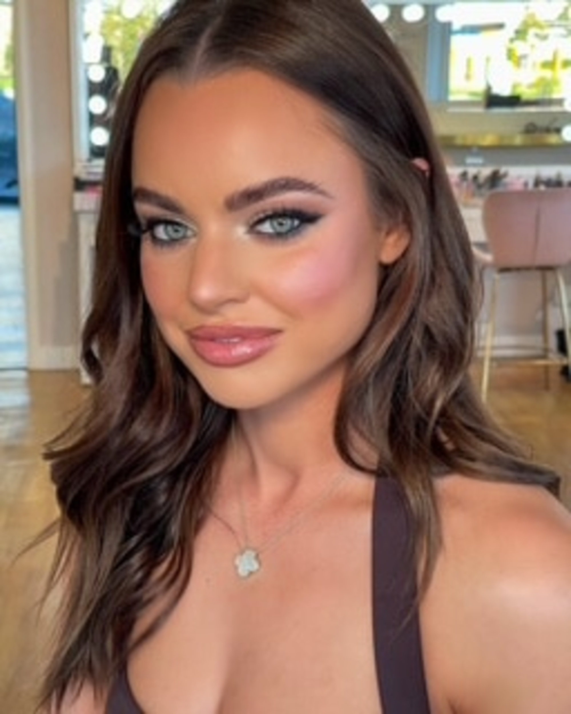 Close-up bridal-style portrait of a woman with glamorous makeup and loose waves in a bright studio.