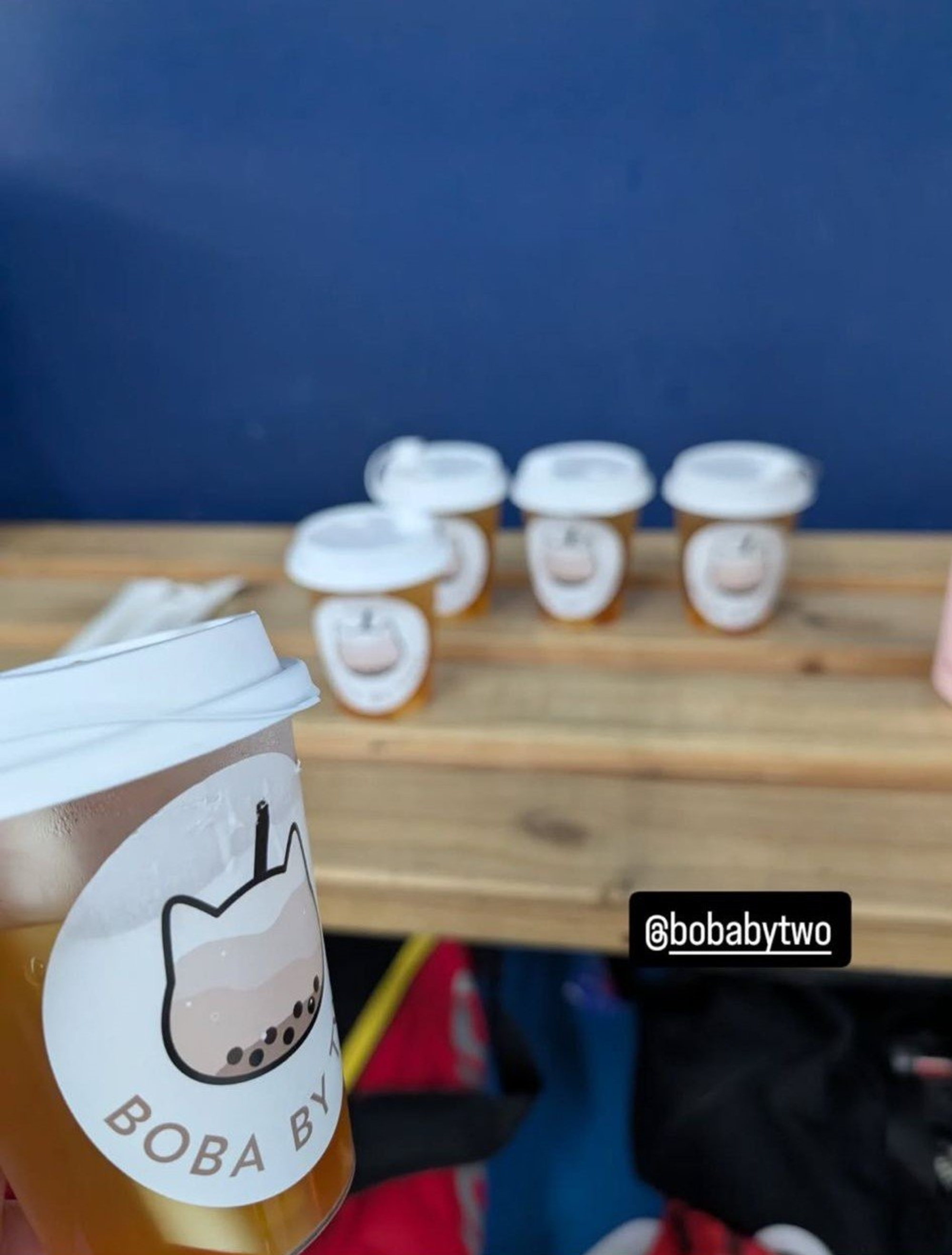 Cups of branded boba tea displayed on a wooden table against a blue wall.