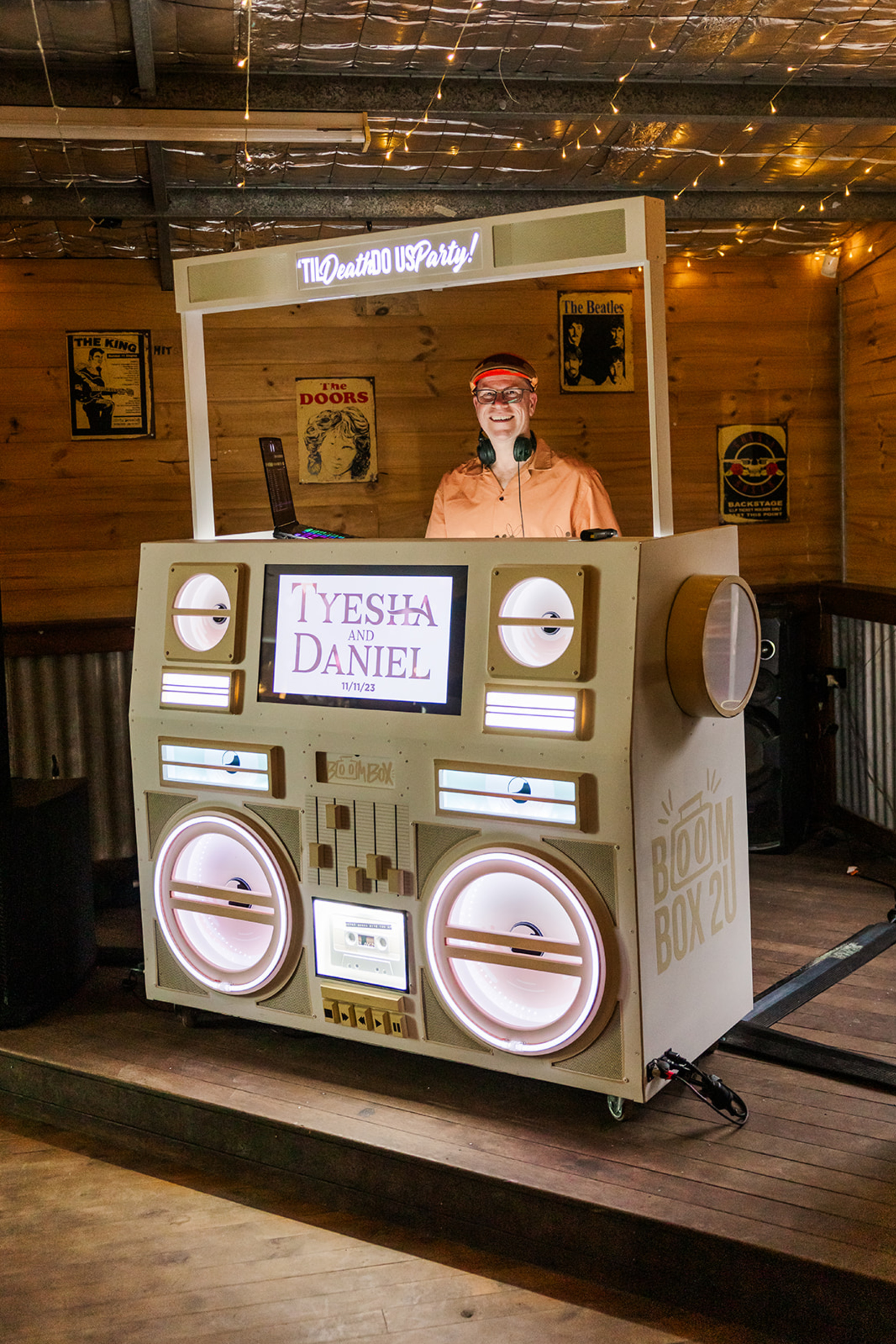 Wedding DJ performing behind a large retro-style boombox booth with custom lighting and couple’s names displayed.