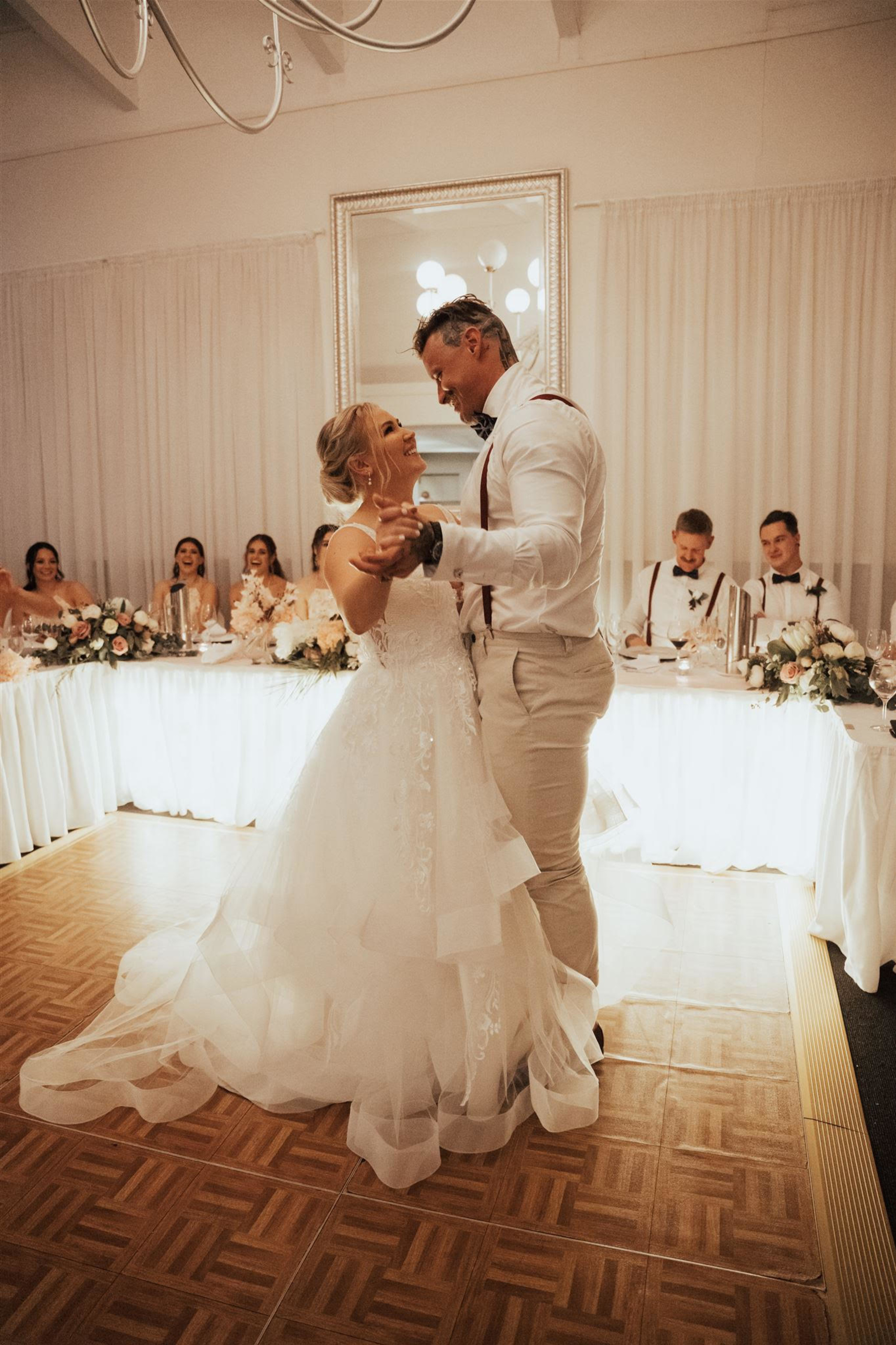 Bride and groom share their first dance in front of the head table at an elegant indoor wedding reception.