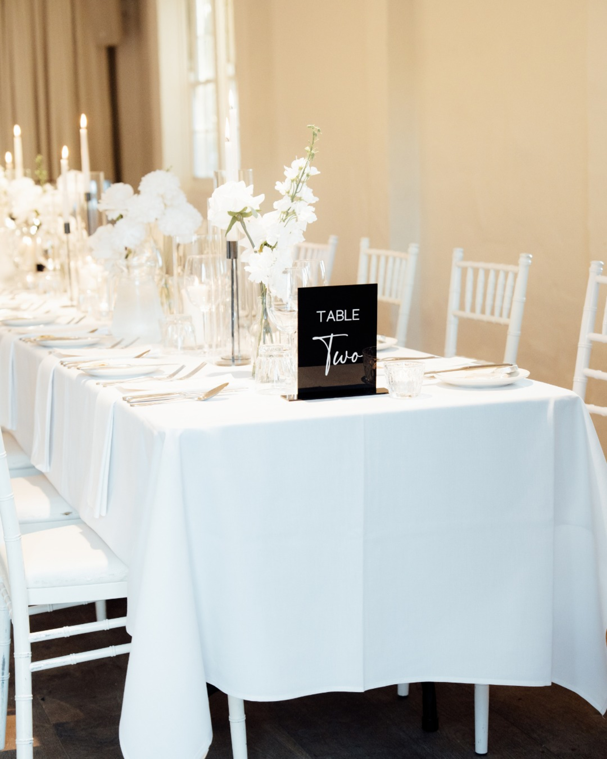 Elegant white wedding reception table with modern black table number sign, white flowers, and candles.