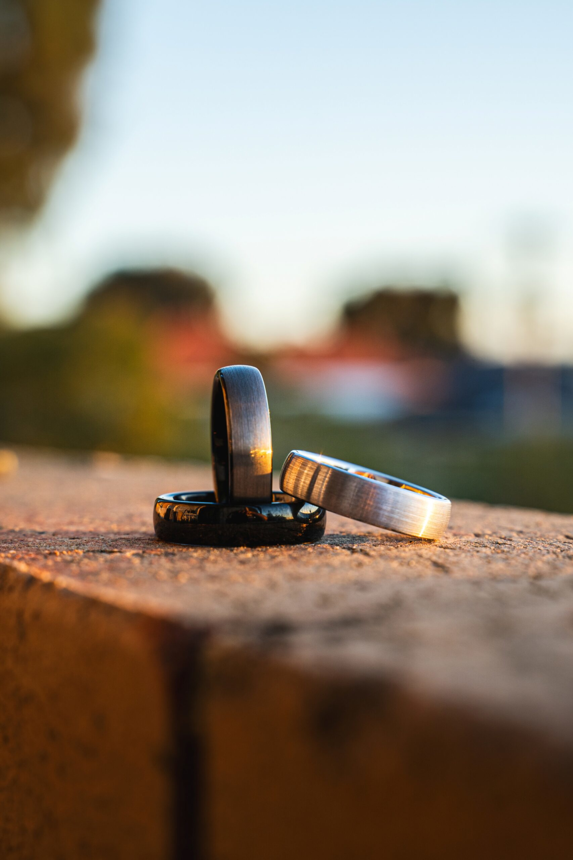 Close-up of three metal wedding bands stacked on a stone surface at sunset with a soft blurred background.