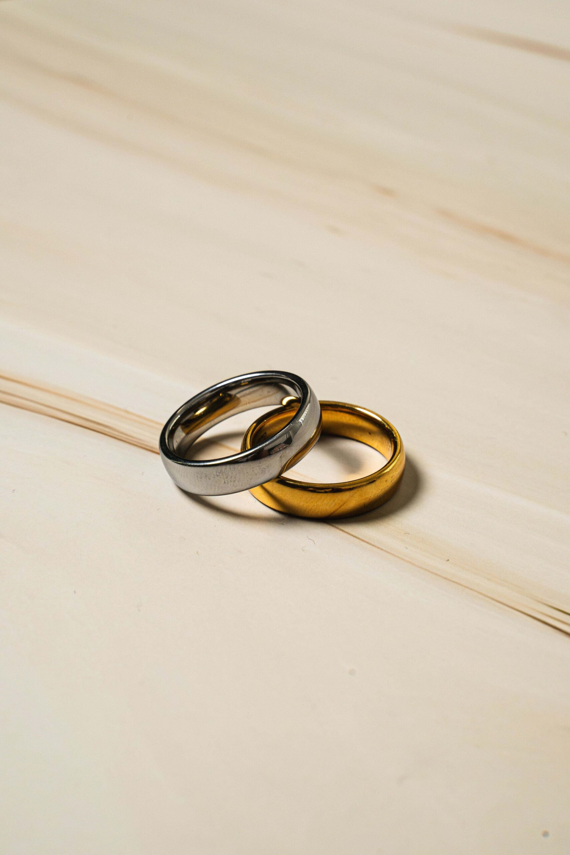 Close-up of intertwined gold and silver wedding bands on a light wooden surface.