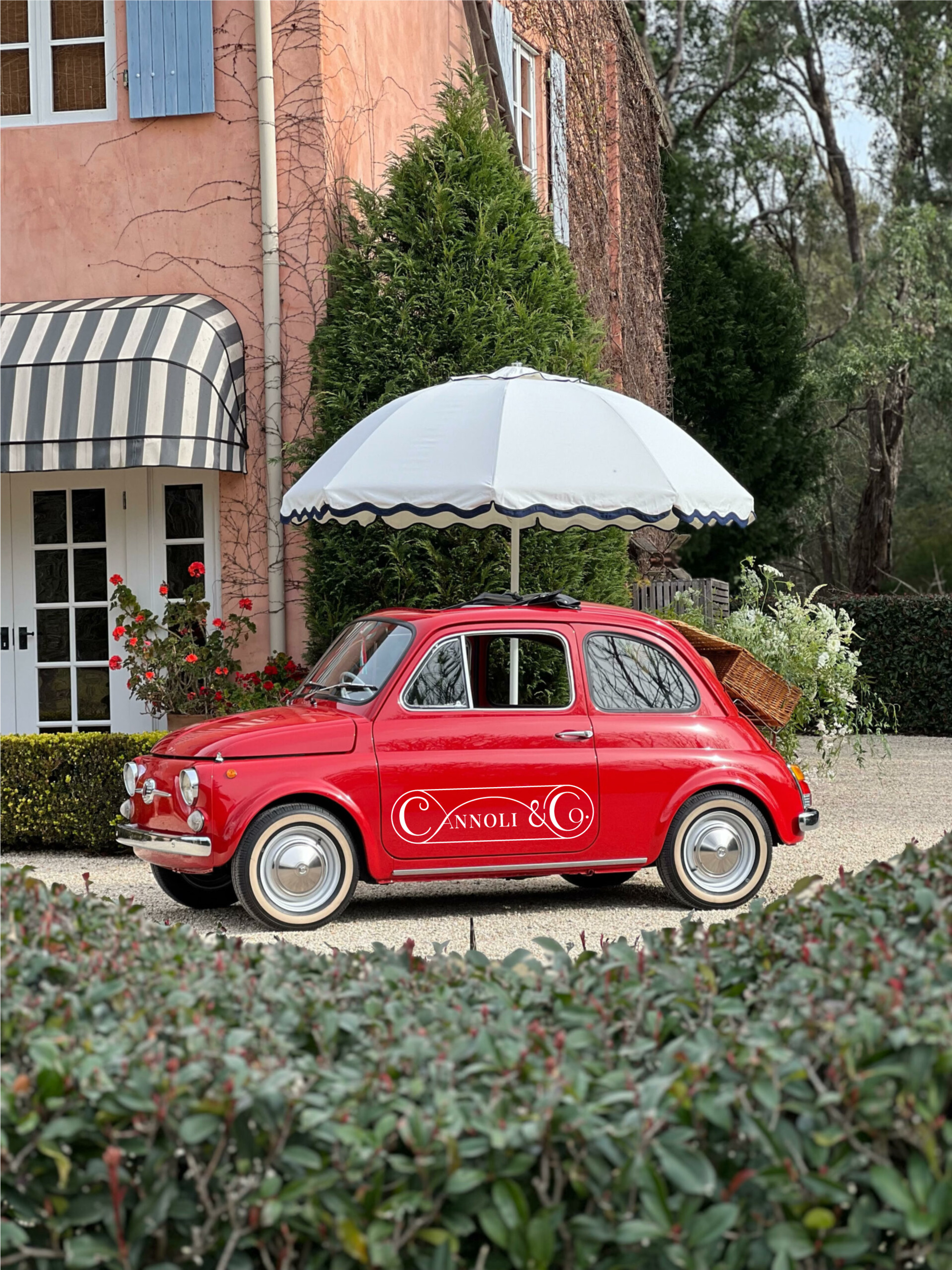 Vintage red cannoli car with umbrella parked by a charming villa for outdoor wedding catering.
