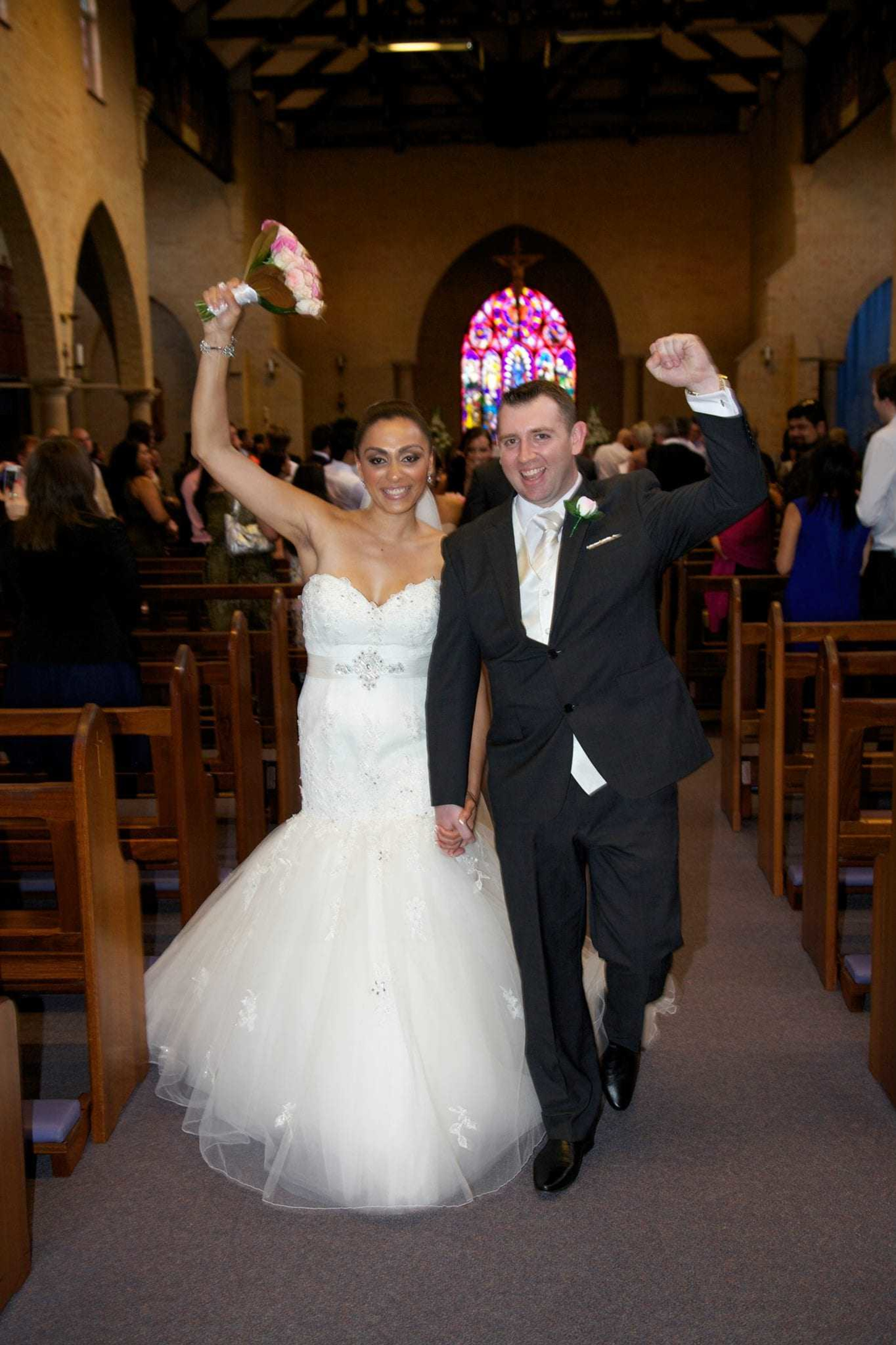 Joyful bride and groom walk up the church aisle holding hands after their wedding ceremony.