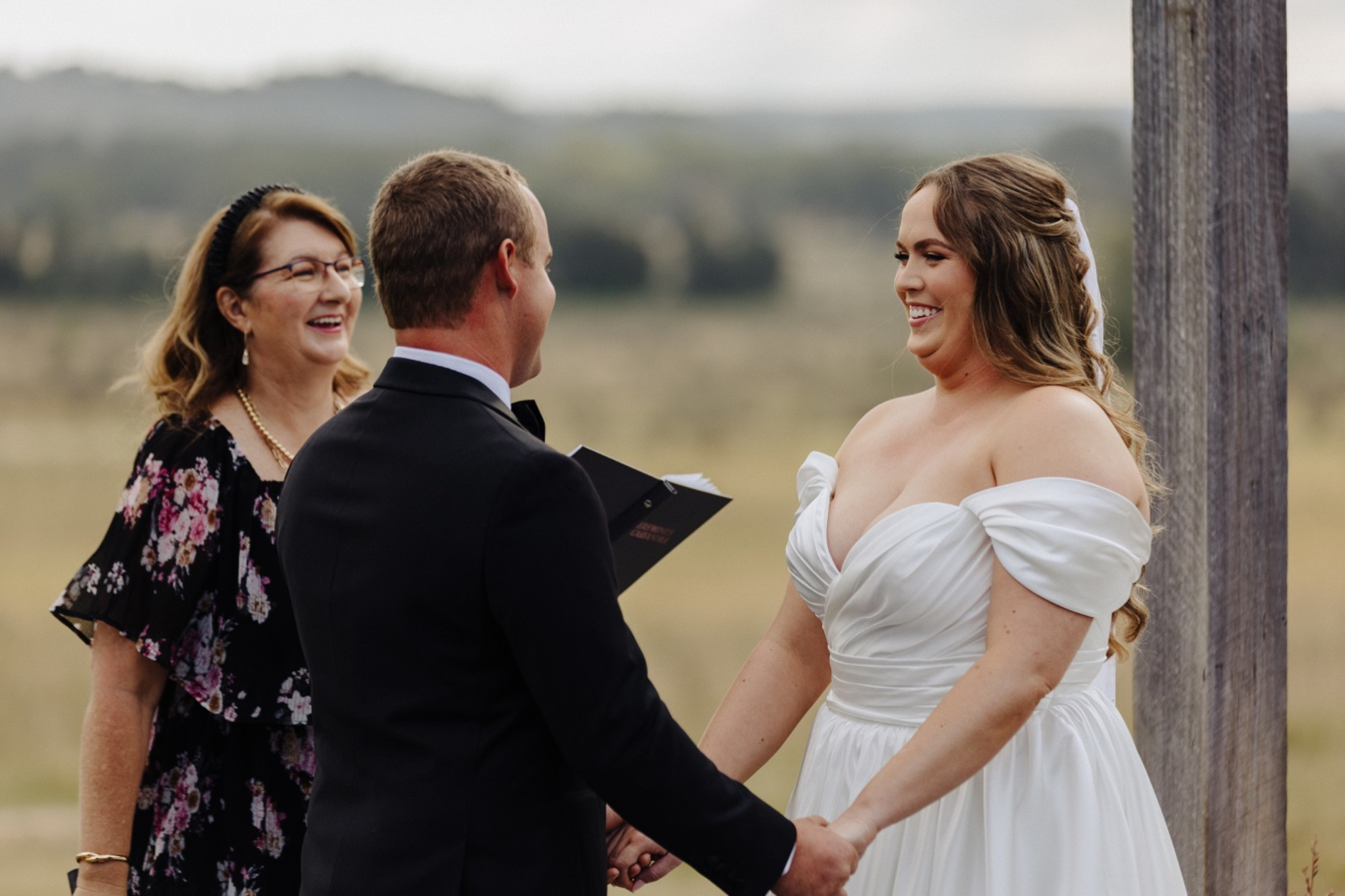 Bride and groom hold hands and smile during an outdoor wedding ceremony with a celebrant.