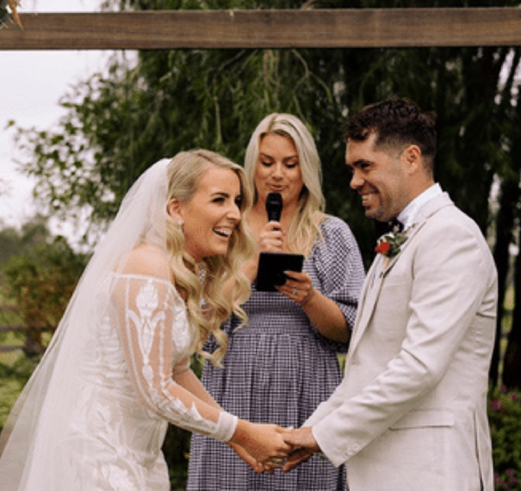 Bride and groom laughing while holding hands during an outdoor ceremony with the officiant reading vows.