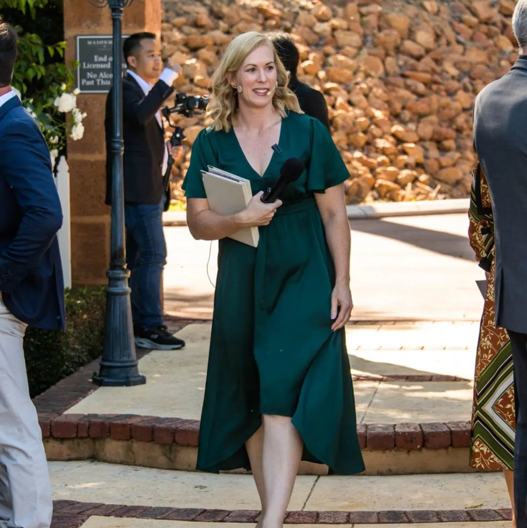 A friendly wedding officiant in a green dress, holding a microphone and notes, ready to lead your ceremony.