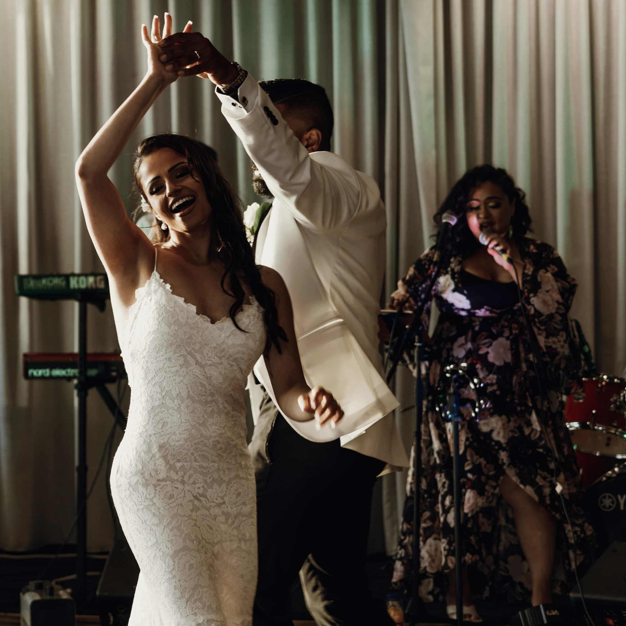 Bride and groom dance joyfully at their wedding reception with a live band performing behind them.