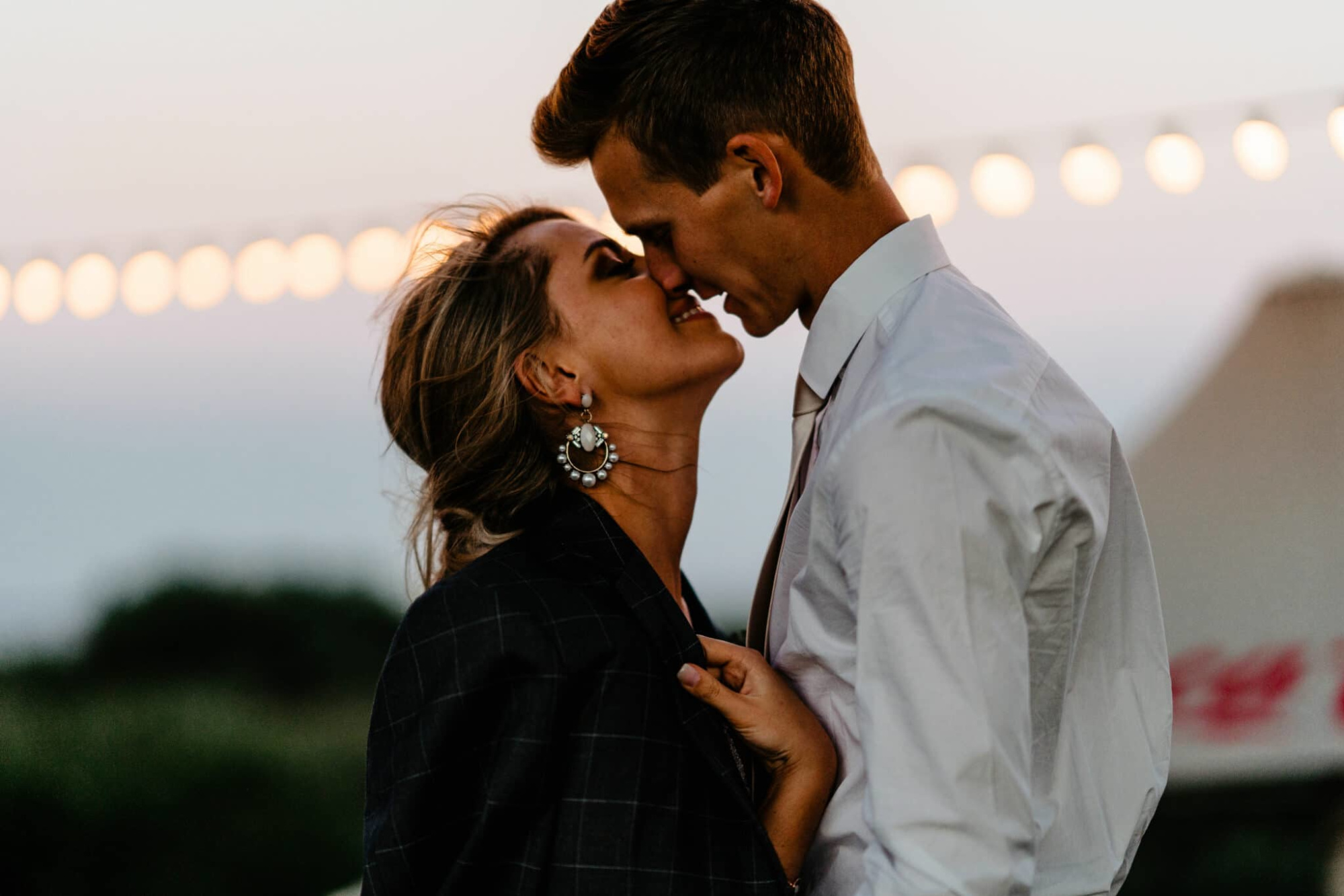 Close-up of a couple sharing an intimate moment under string lights at an outdoor evening wedding.