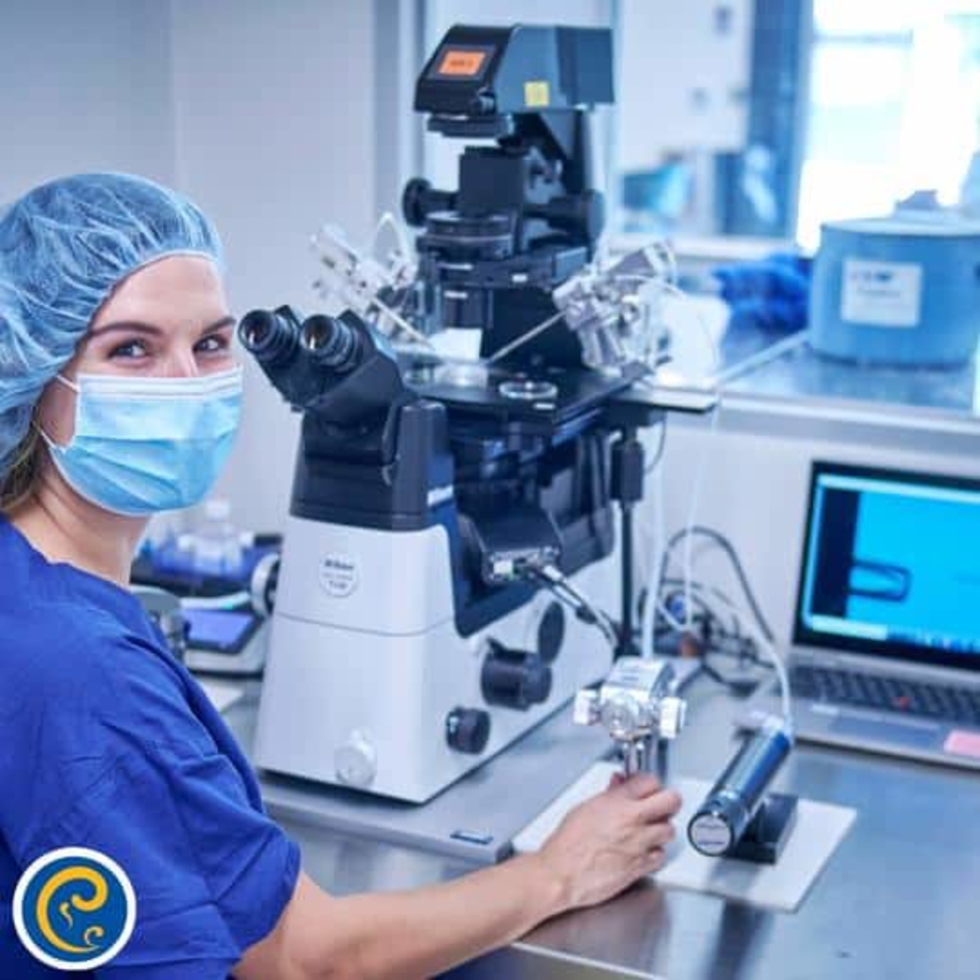 Scientist in scrubs and mask working at an advanced microscope in a modern laboratory.