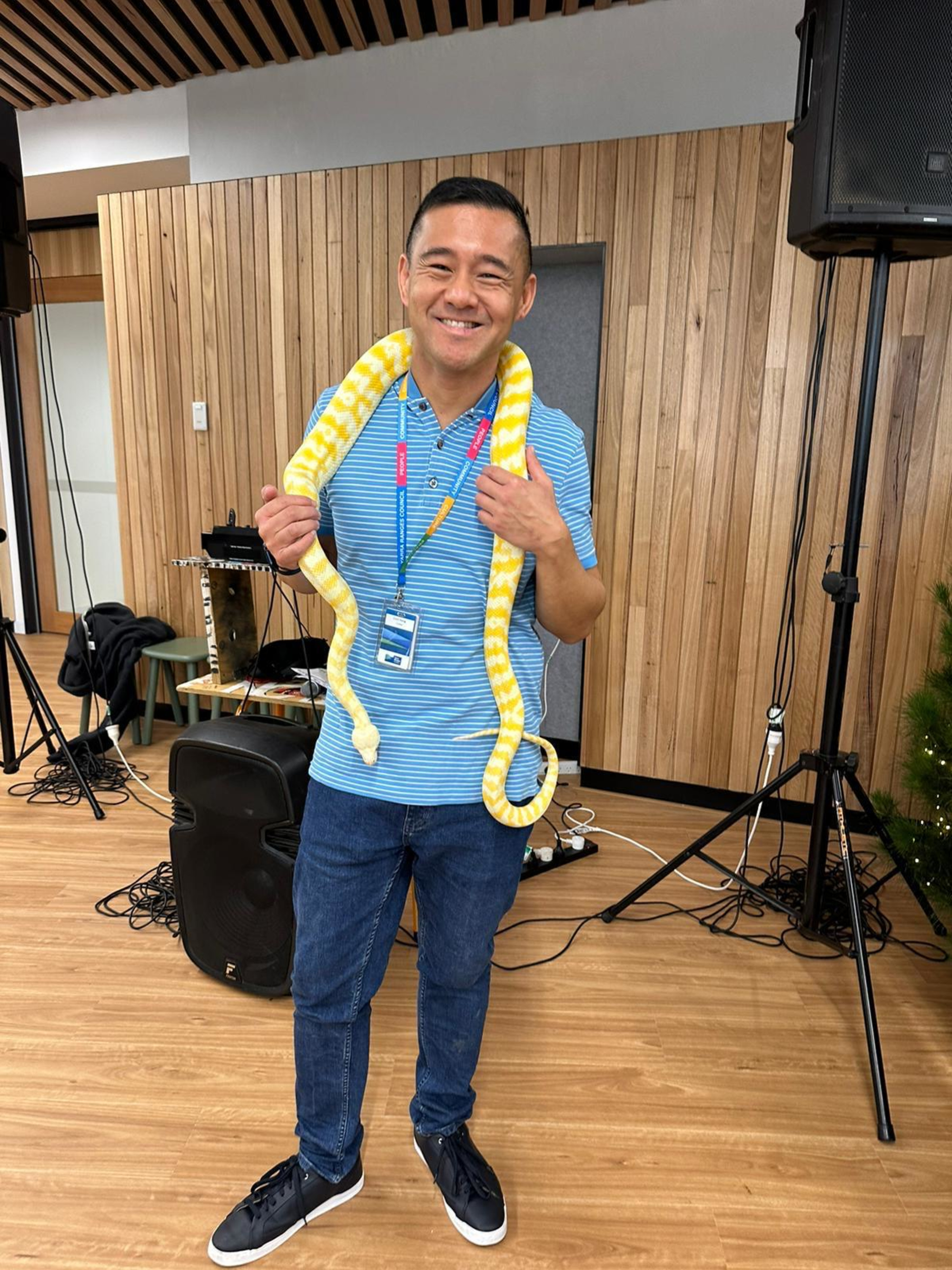 Person smiling indoors while holding a yellow and white snake around their shoulders.