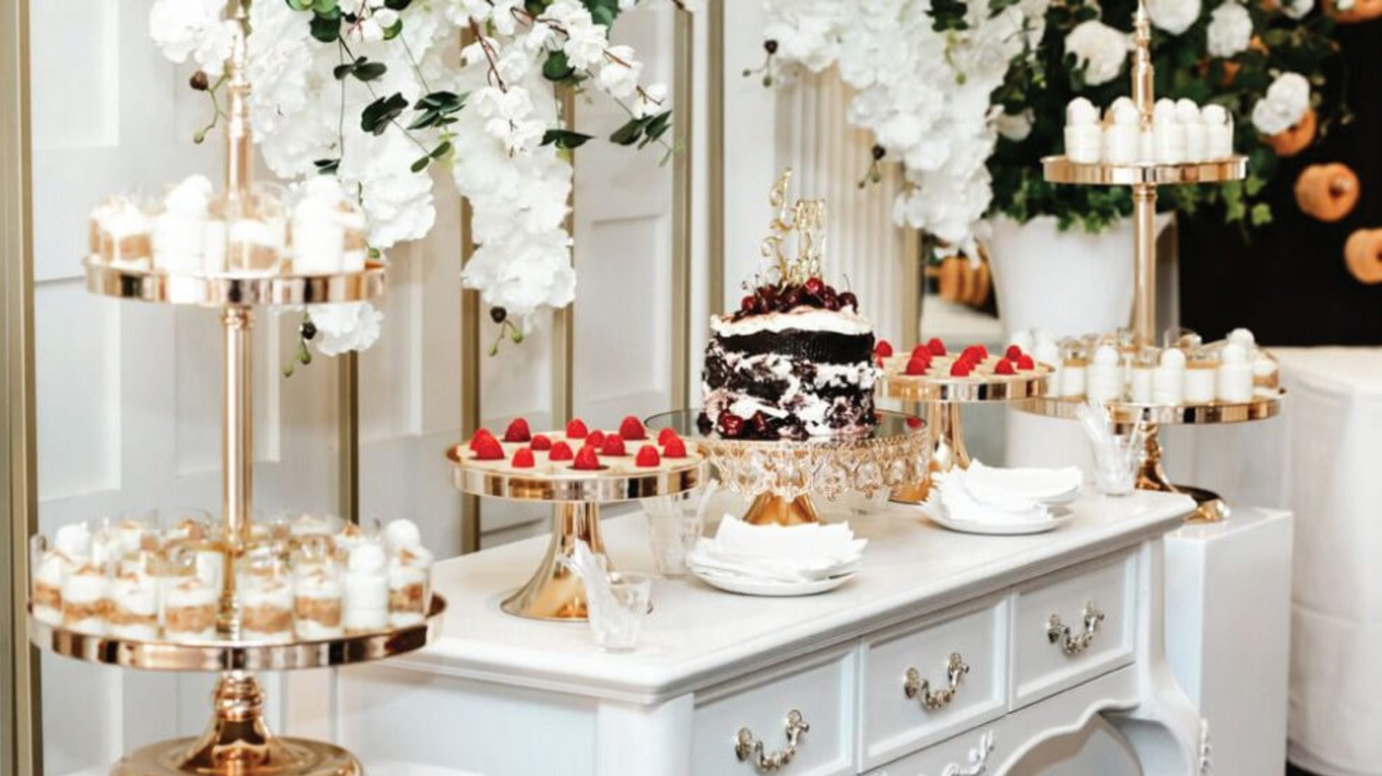 Elegant white and gold wedding dessert table with tiered stands, floral decor, and a centerpiece cake.