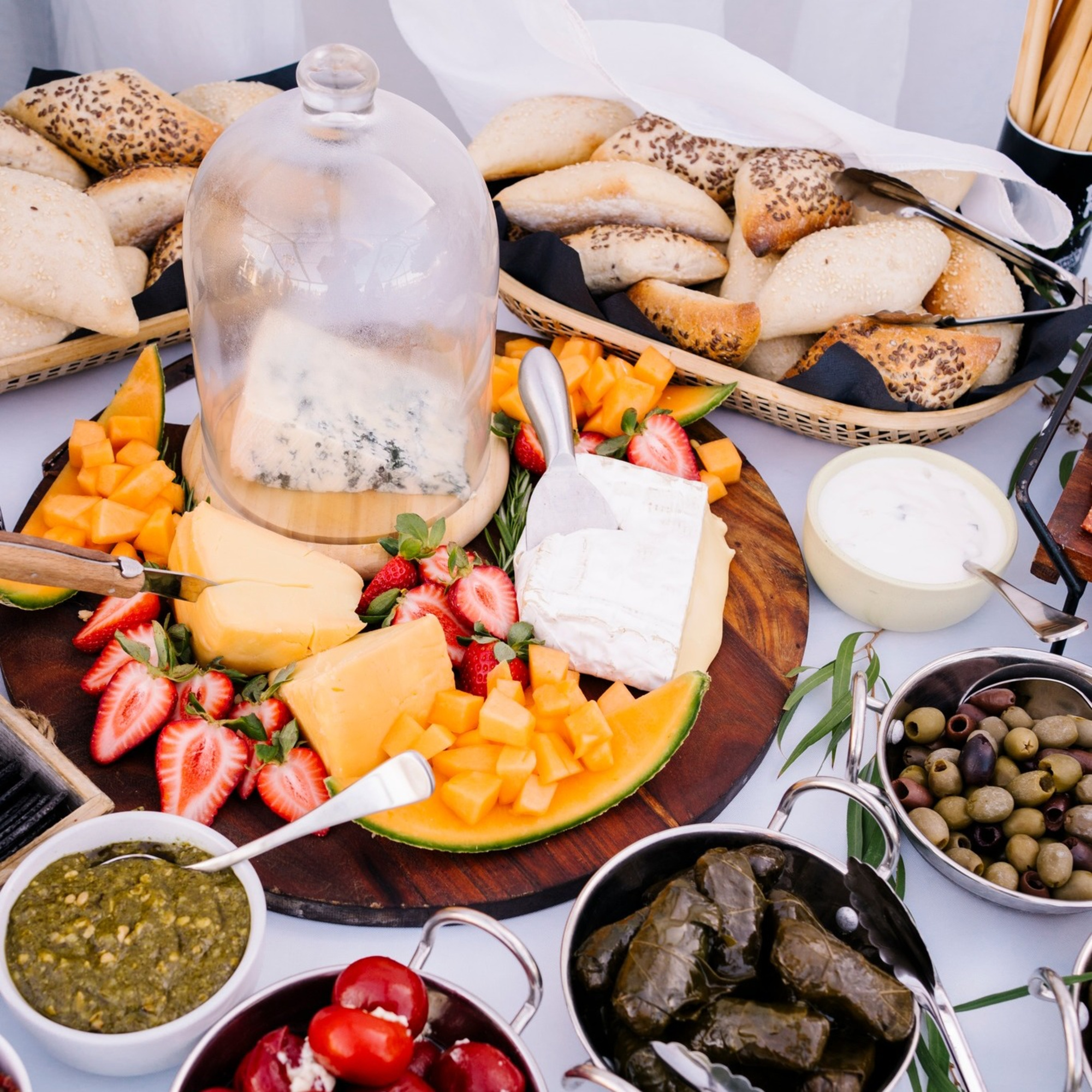 Elegant wedding grazing table with assorted cheeses, fruit, bread, olives, and dips arranged on a wooden board.