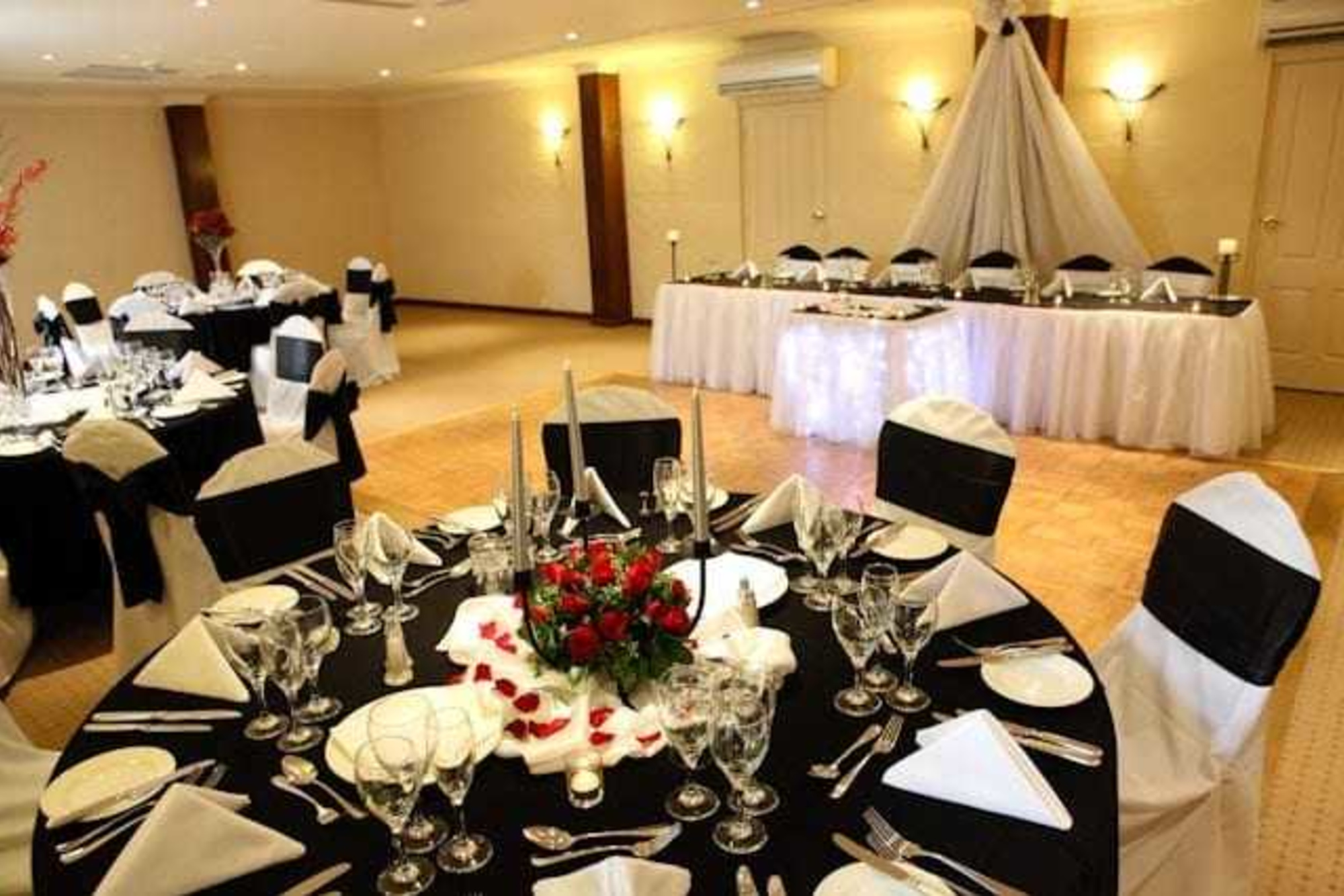 Elegant indoor wedding reception setup with black and white linens and red rose centerpieces.
