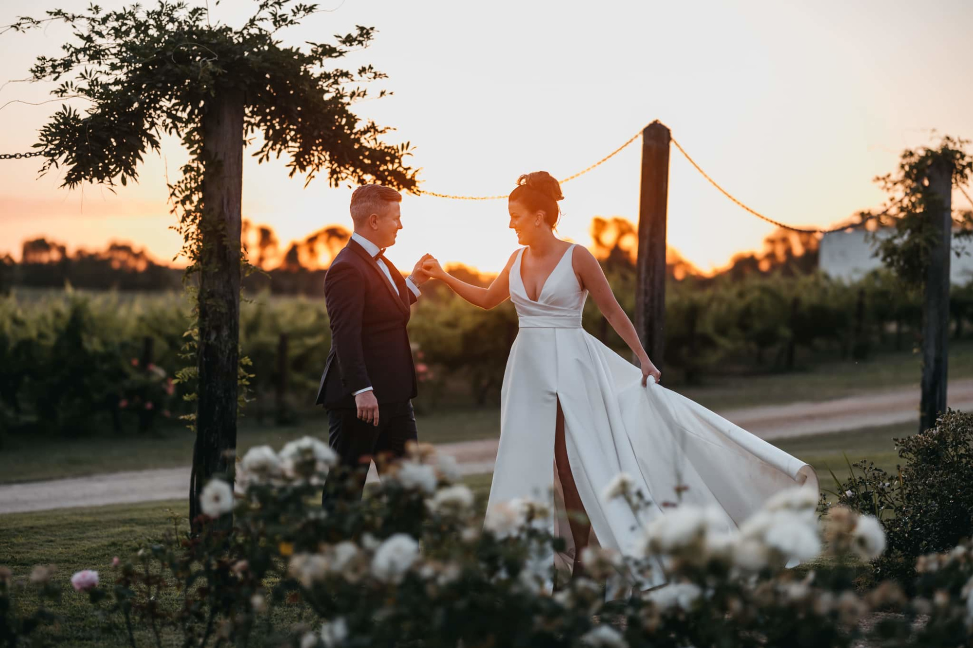 Bride and groom share a romantic moment in a vineyard garden at sunset.