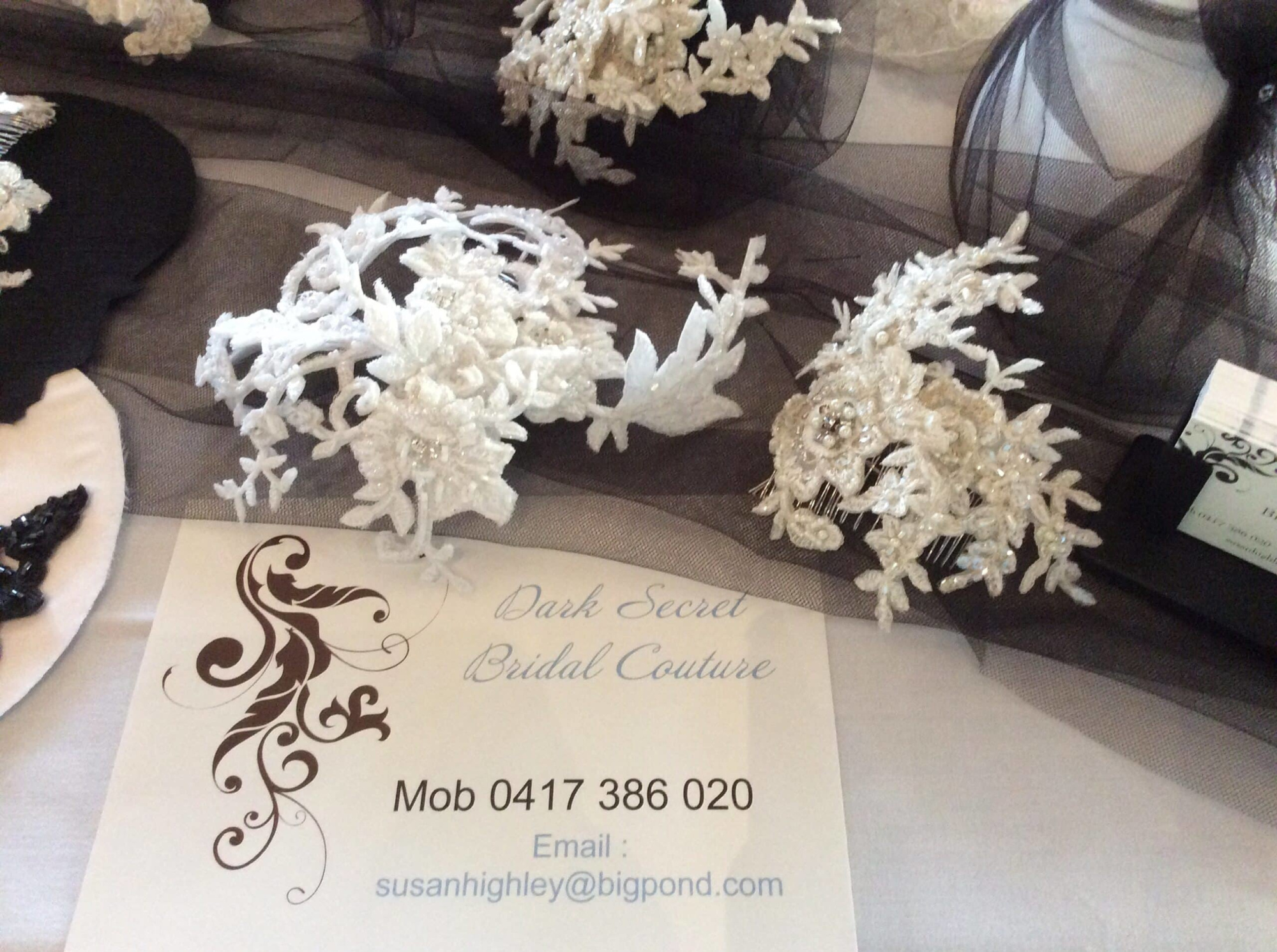 Delicate lace and beaded bridal hairpieces displayed on dark tulle beside a bridal couture business card.
