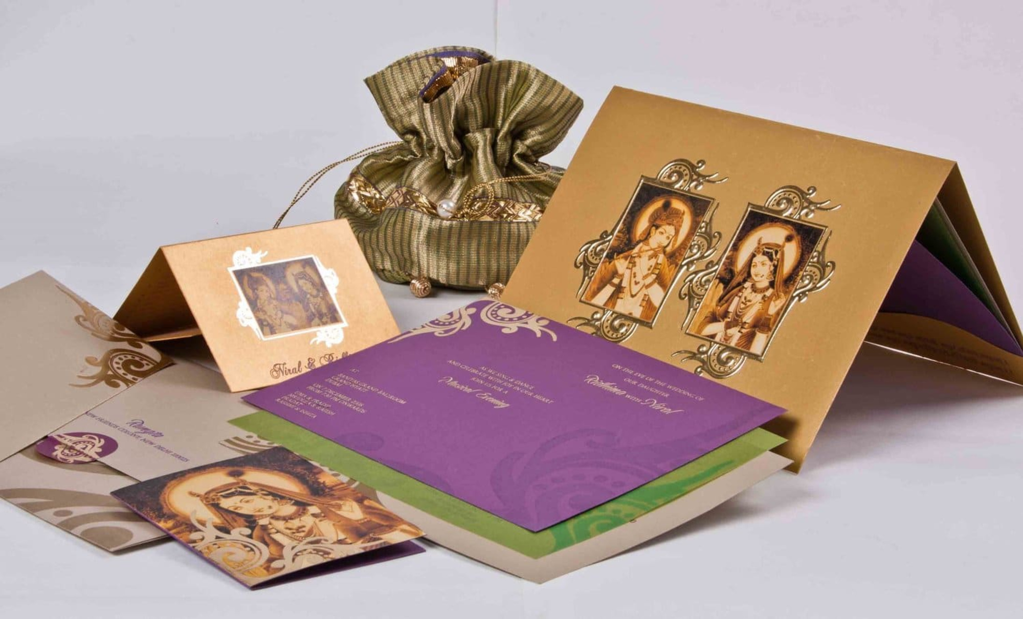 Assorted traditional Indian wedding invitation cards with religious artwork and ornate designs displayed with a decorative pouch.