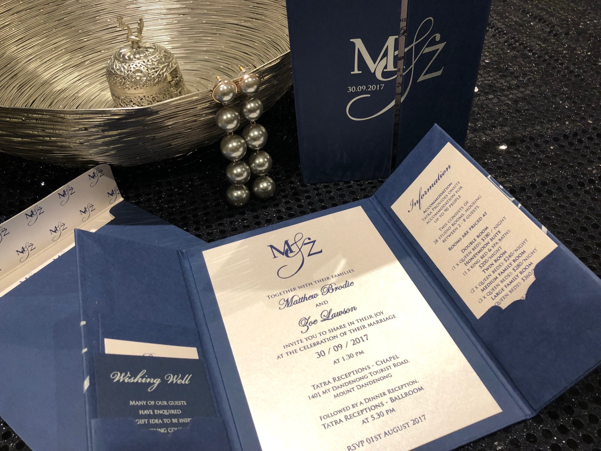 Elegant navy and cream wedding invitation suite displayed with silver bowl and pearl earrings.