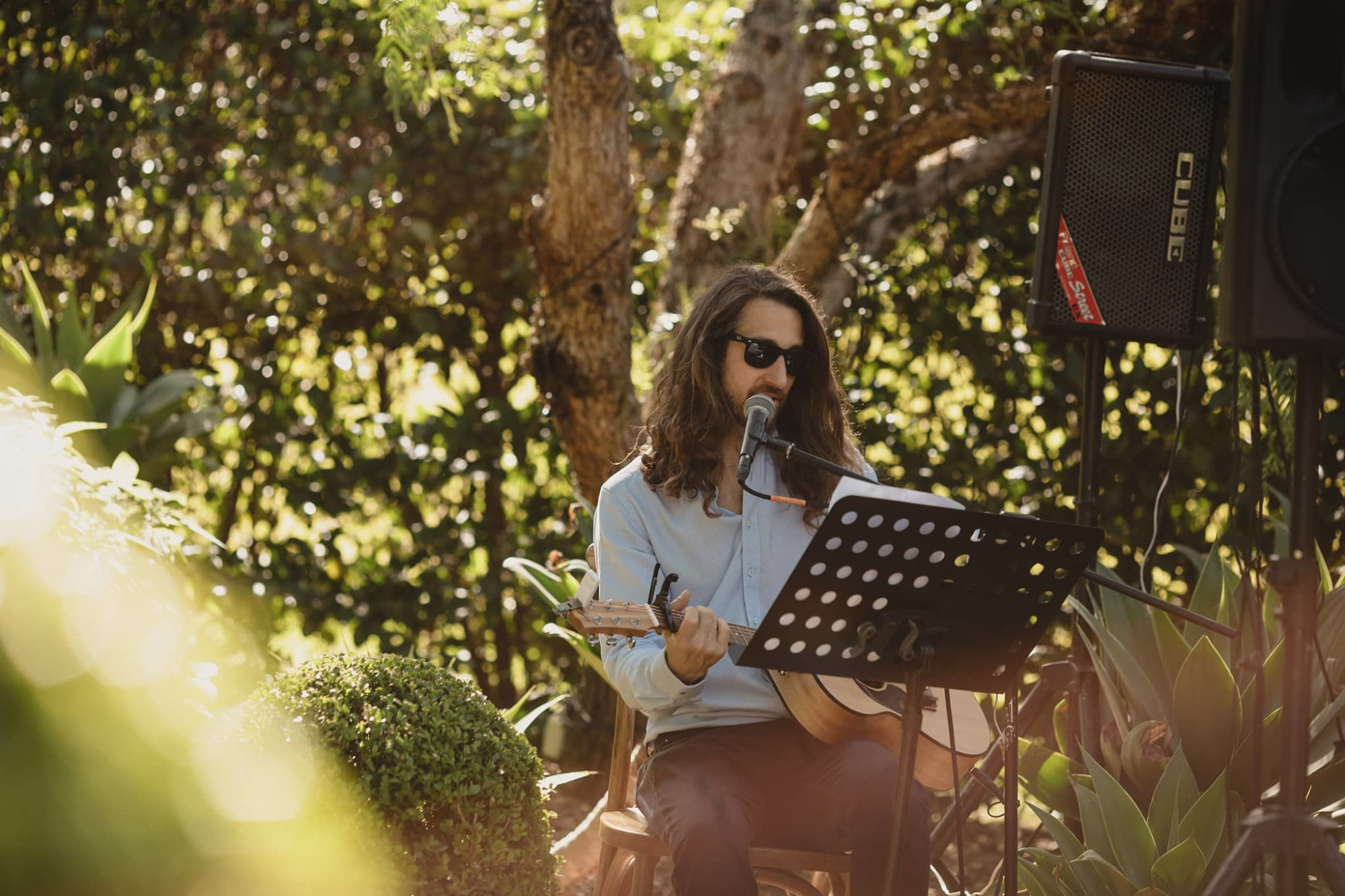 Acoustic musician with guitar singing into a microphone at an outdoor garden wedding setup.