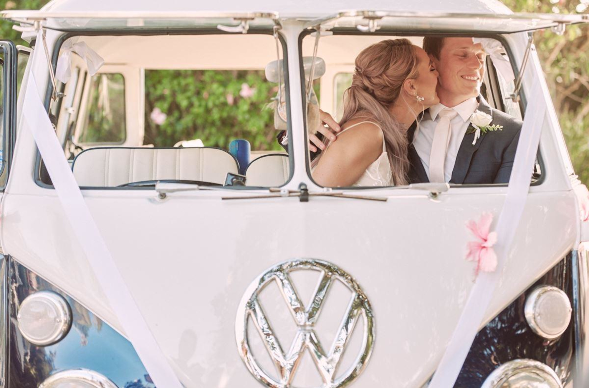 Newlywed couple shares a kiss inside a decorated vintage VW van used as their wedding car.