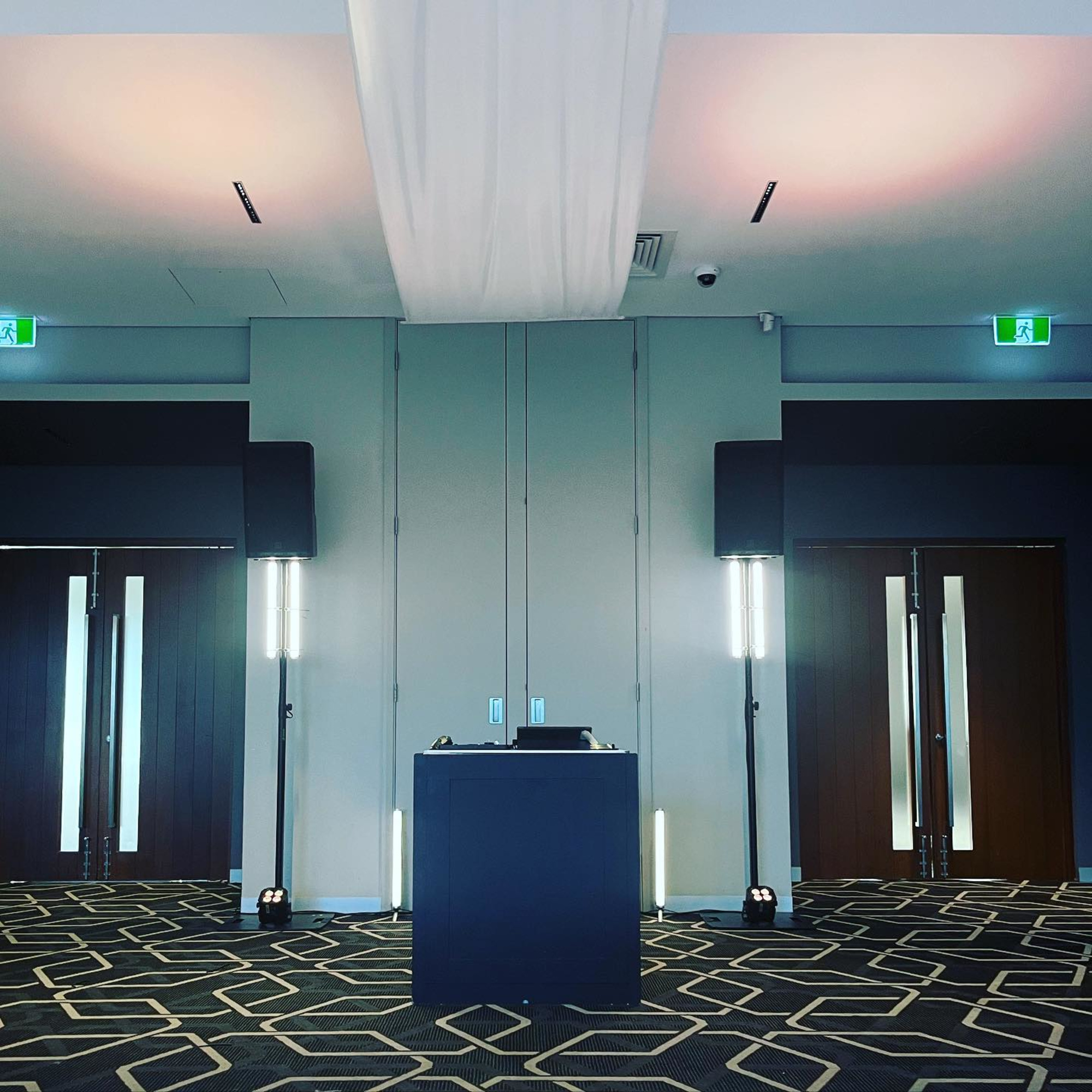 Modern indoor wedding venue setup with central DJ booth and geometric carpet design