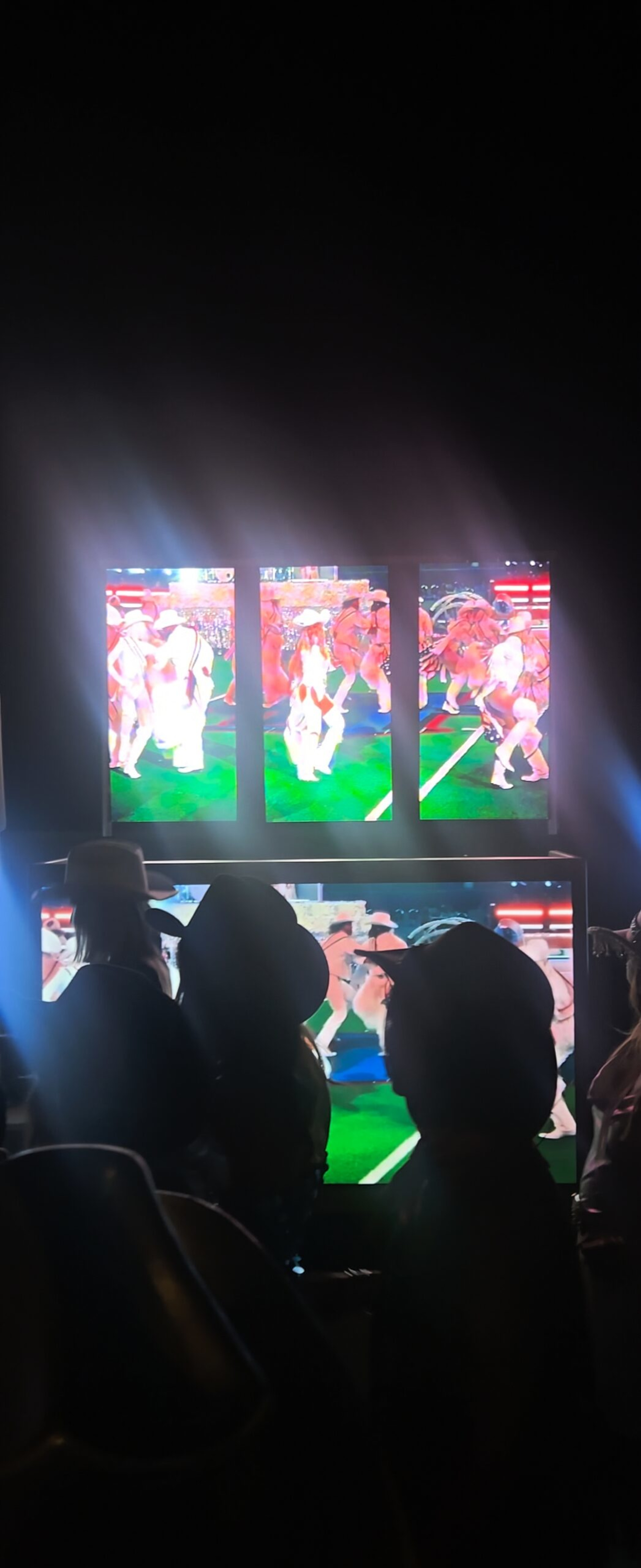 Guests in cowboy hats watch dancers on a bright multi-screen video wall at a nighttime wedding reception.