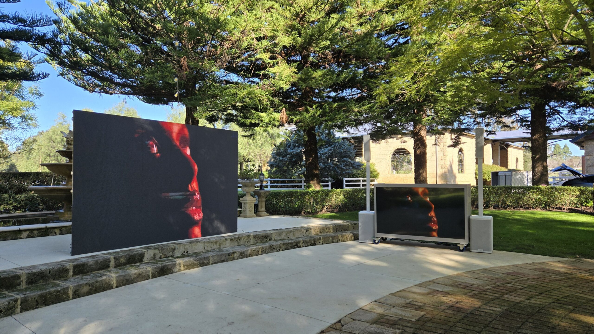 Outdoor wedding venue with large video screens set up in a garden courtyard.
