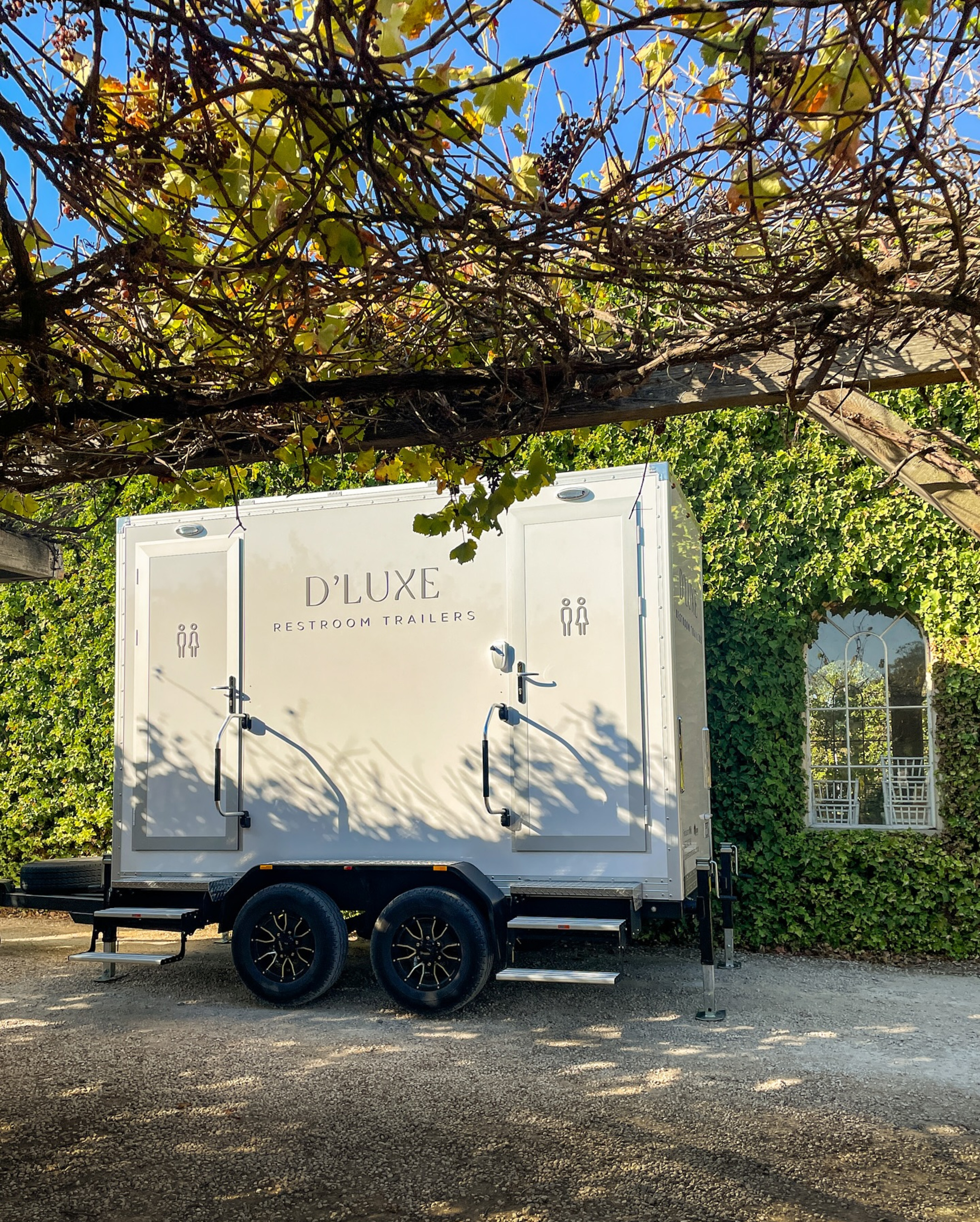 Luxury restroom trailer parked at an ivy-covered outdoor wedding venue under a vine-covered pergola.
