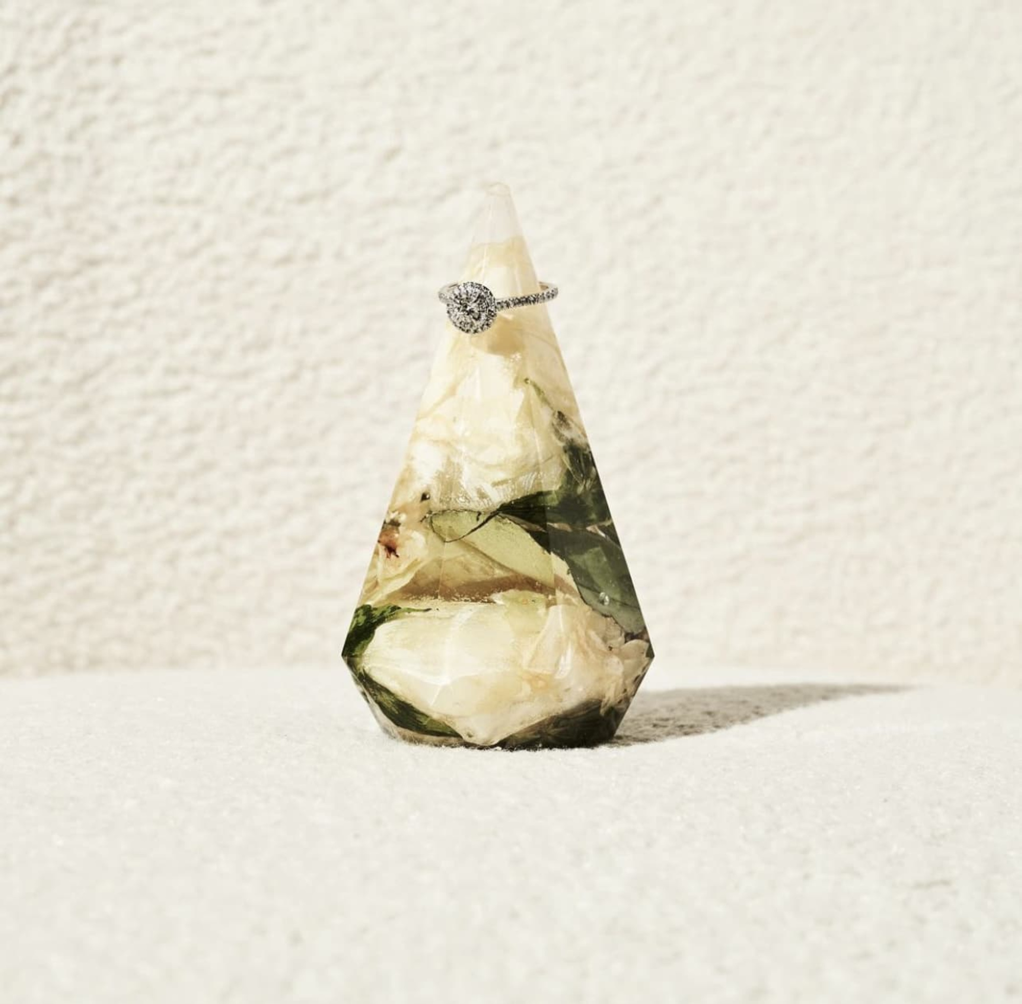 Diamond engagement ring displayed on a floral resin geometric ring holder against a neutral background.