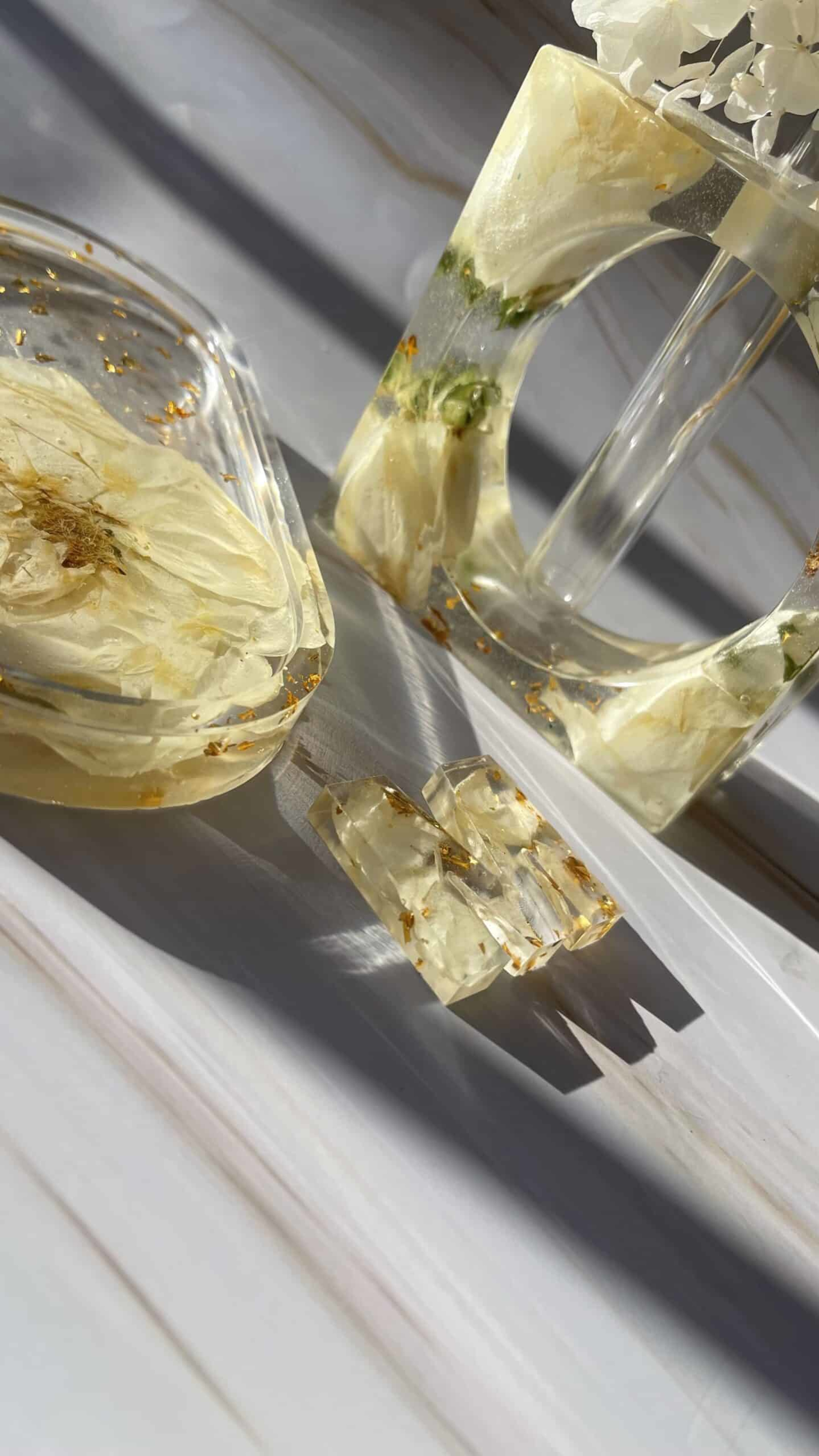 Sunlit resin pieces with preserved white florals and gold flakes displayed on a light marble surface.