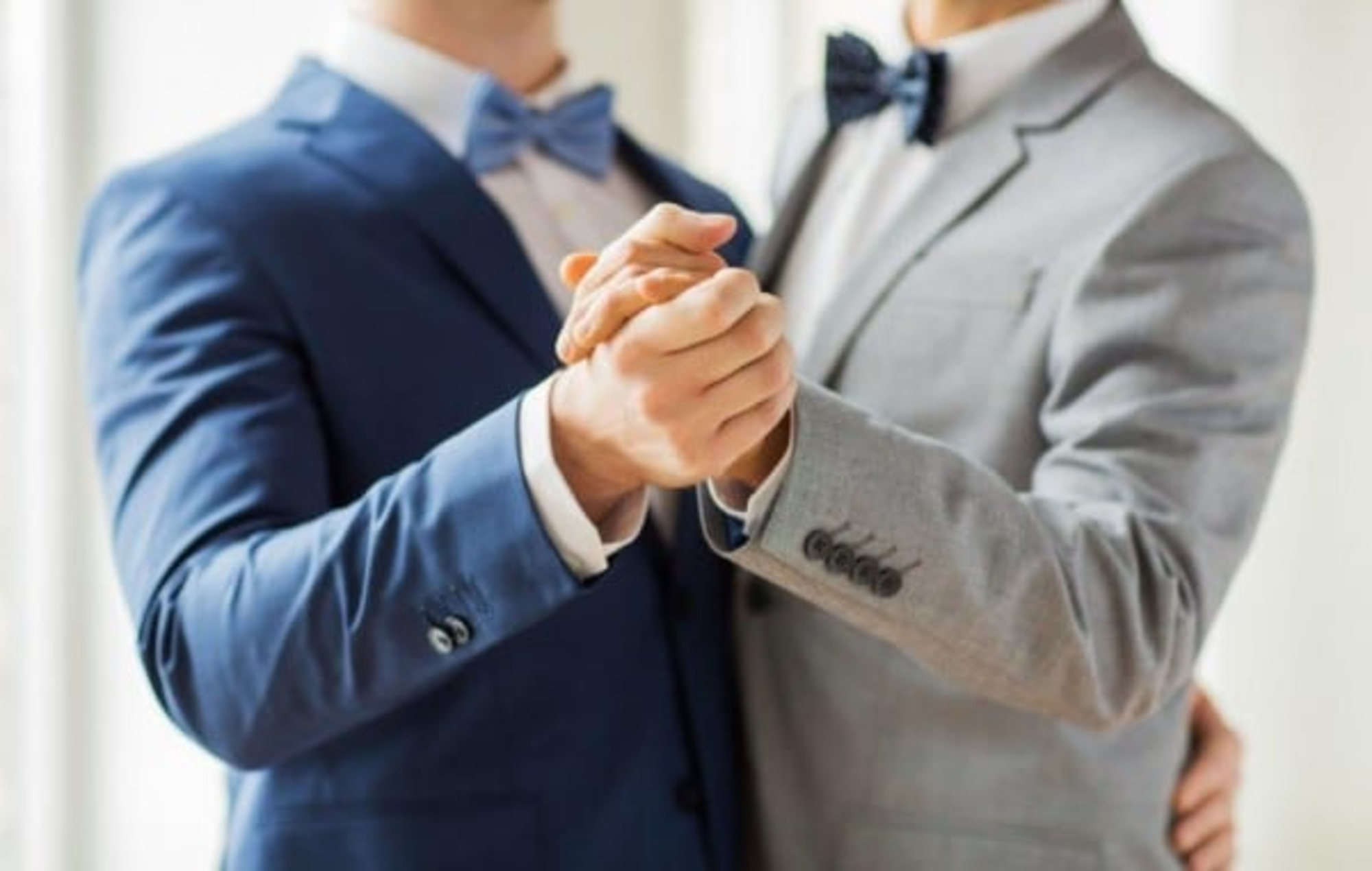 Two grooms in suits holding hands while dancing at their wedding.