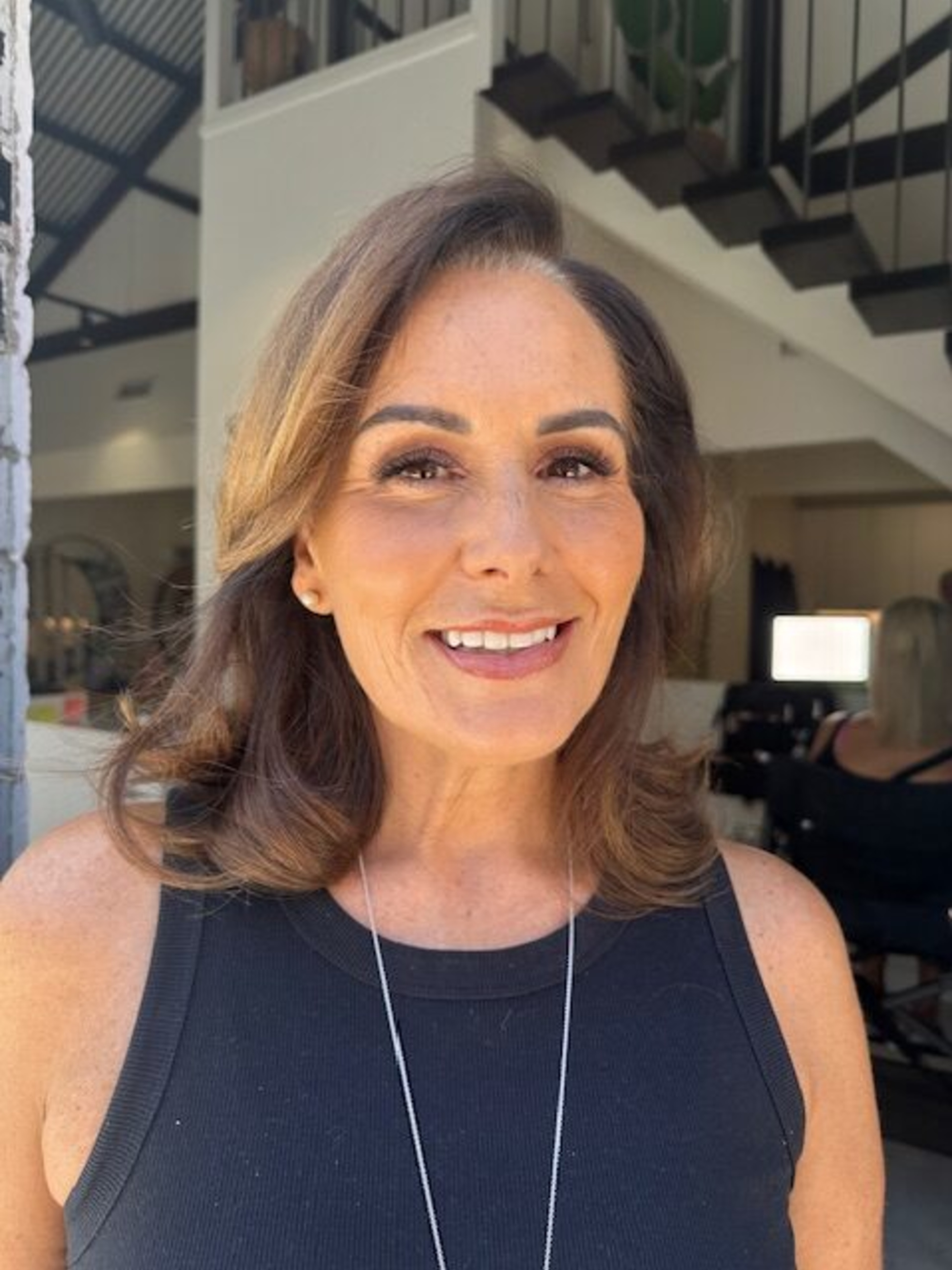 Smiling woman with natural glam makeup and styled hair posing indoors in a bright studio setting.