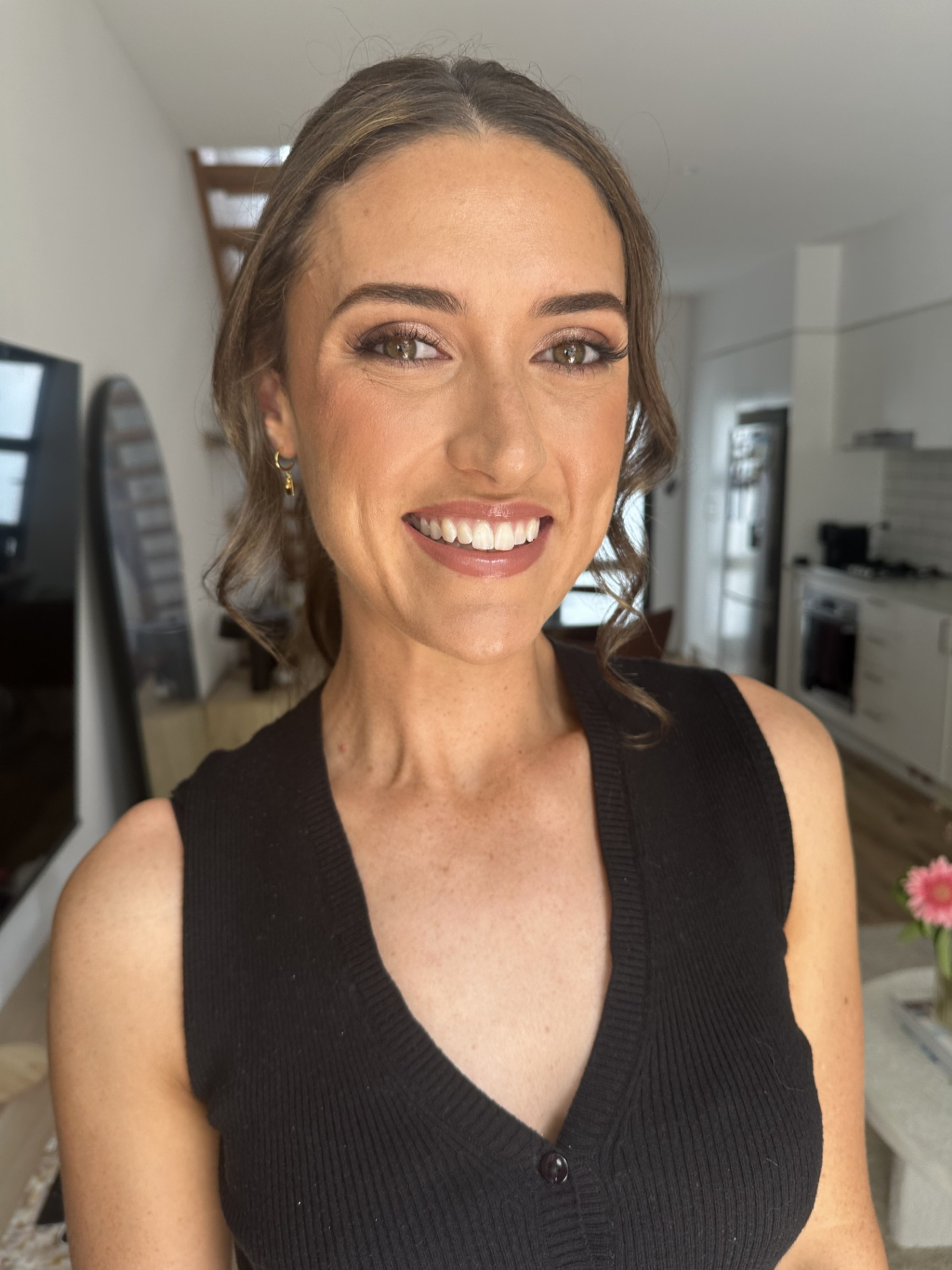 Close-up portrait of a woman with soft bridal makeup and styled hair standing in a bright modern room.