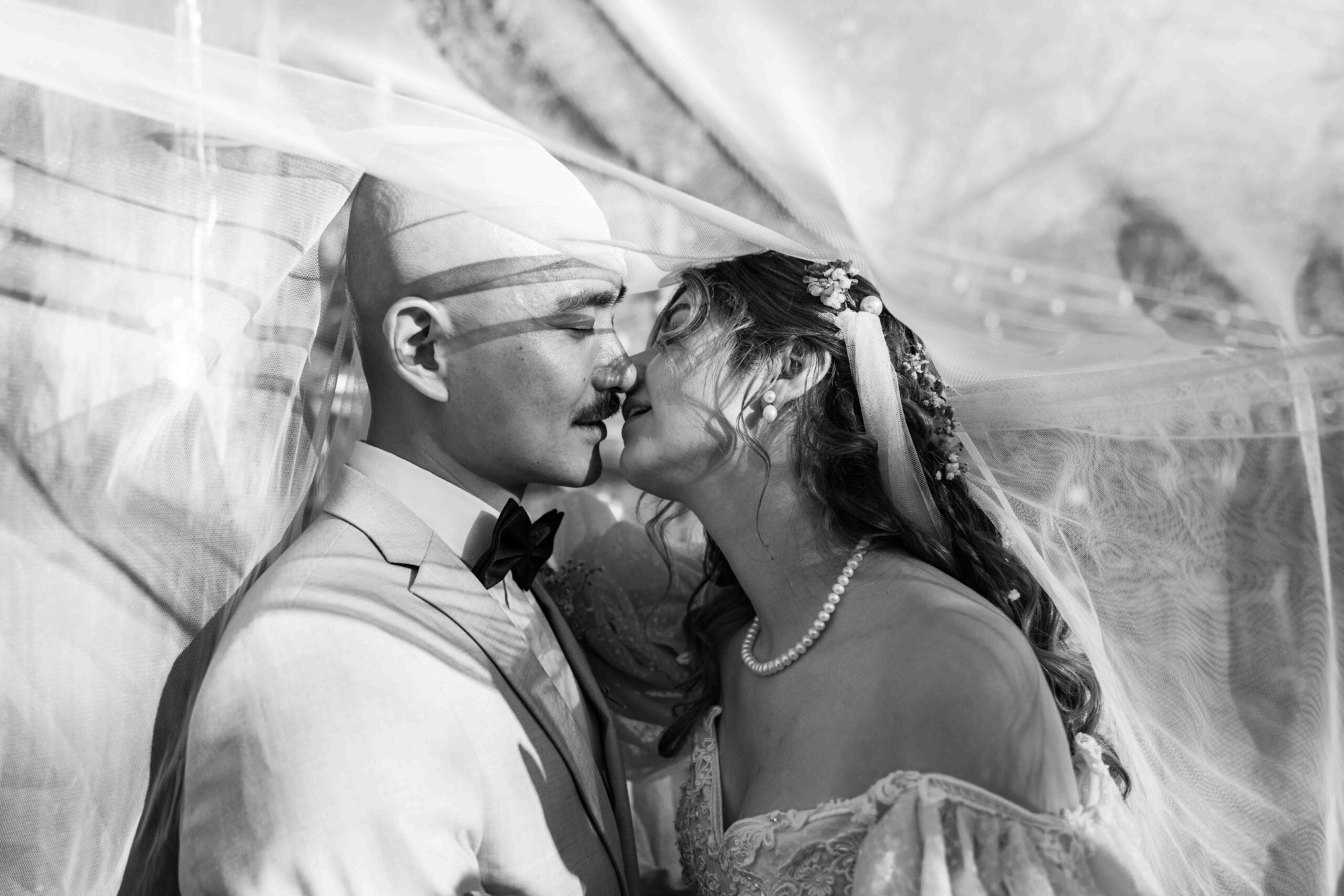 Black and white close-up of a bride and groom sharing an intimate moment beneath a flowing veil.