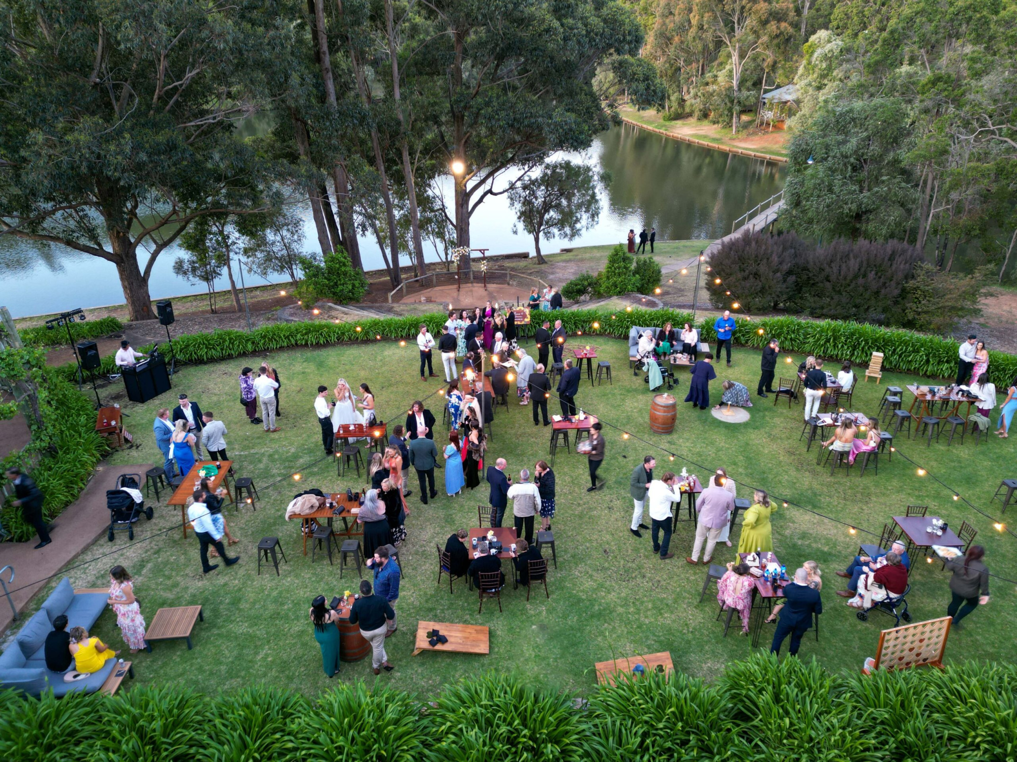 Aerial view of a lakeside garden wedding reception with guests mingling under string lights.
