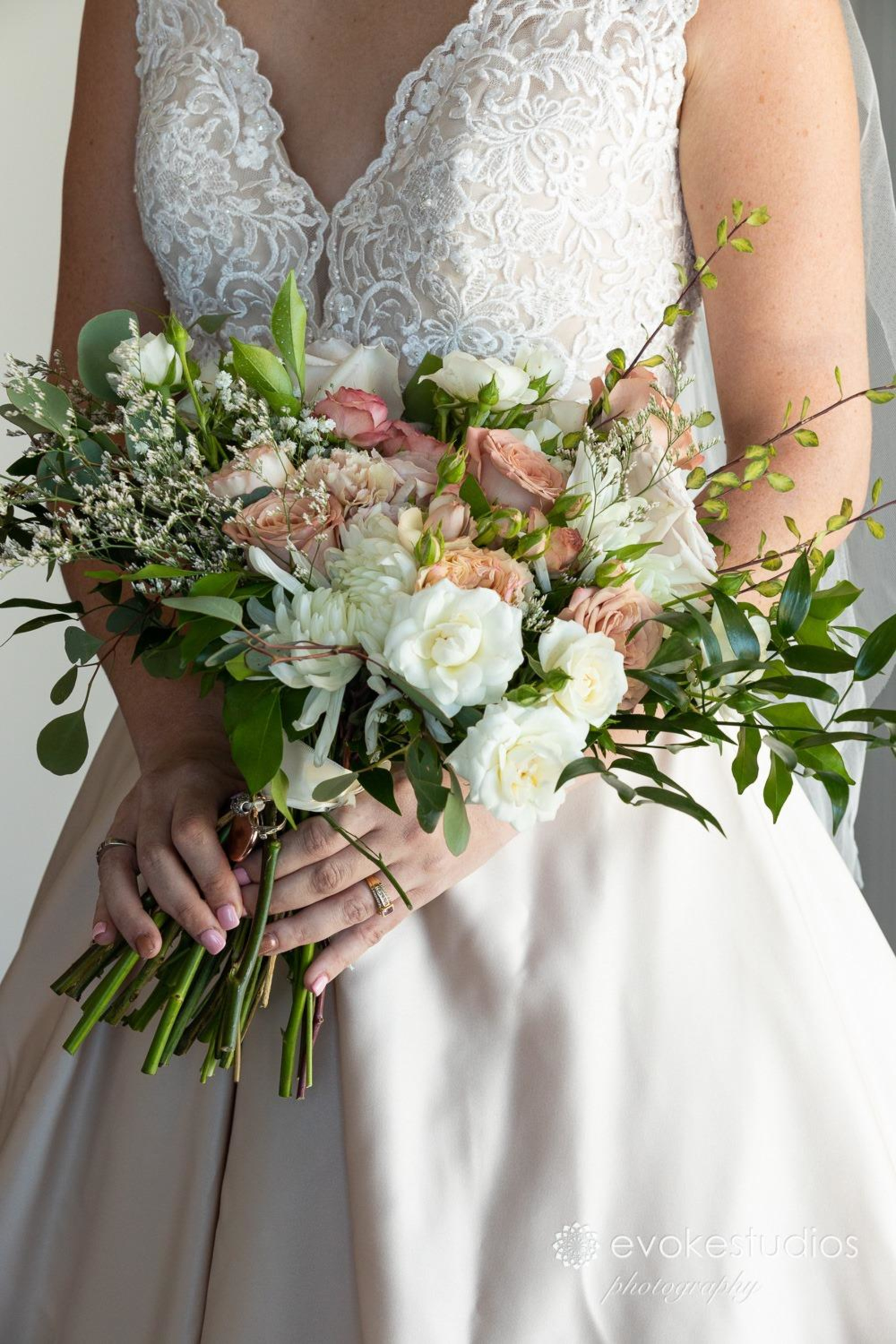 Bride in a lace gown holding a lush bouquet of white and blush flowers with greenery.