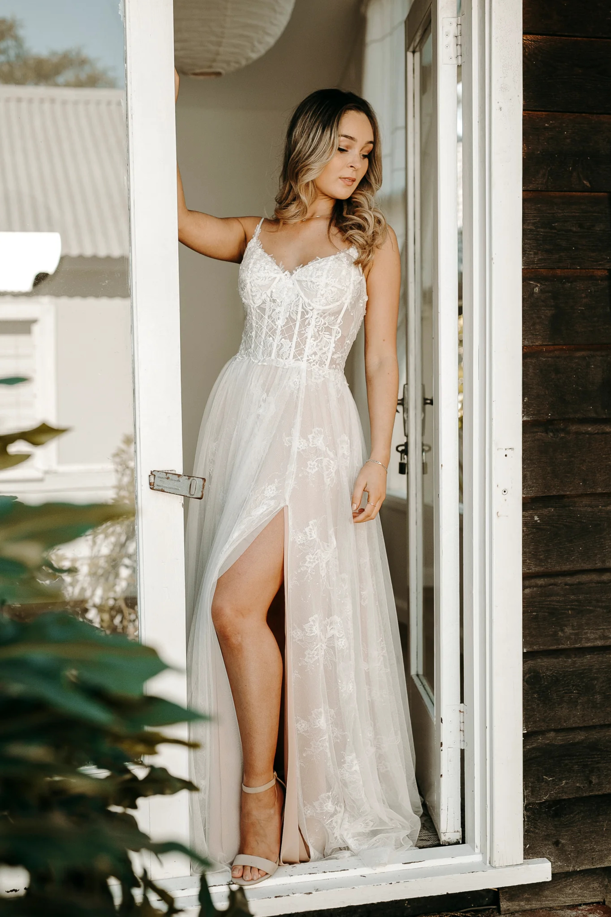 Bride in a lace wedding dress with a thigh-high slit standing in a doorway.