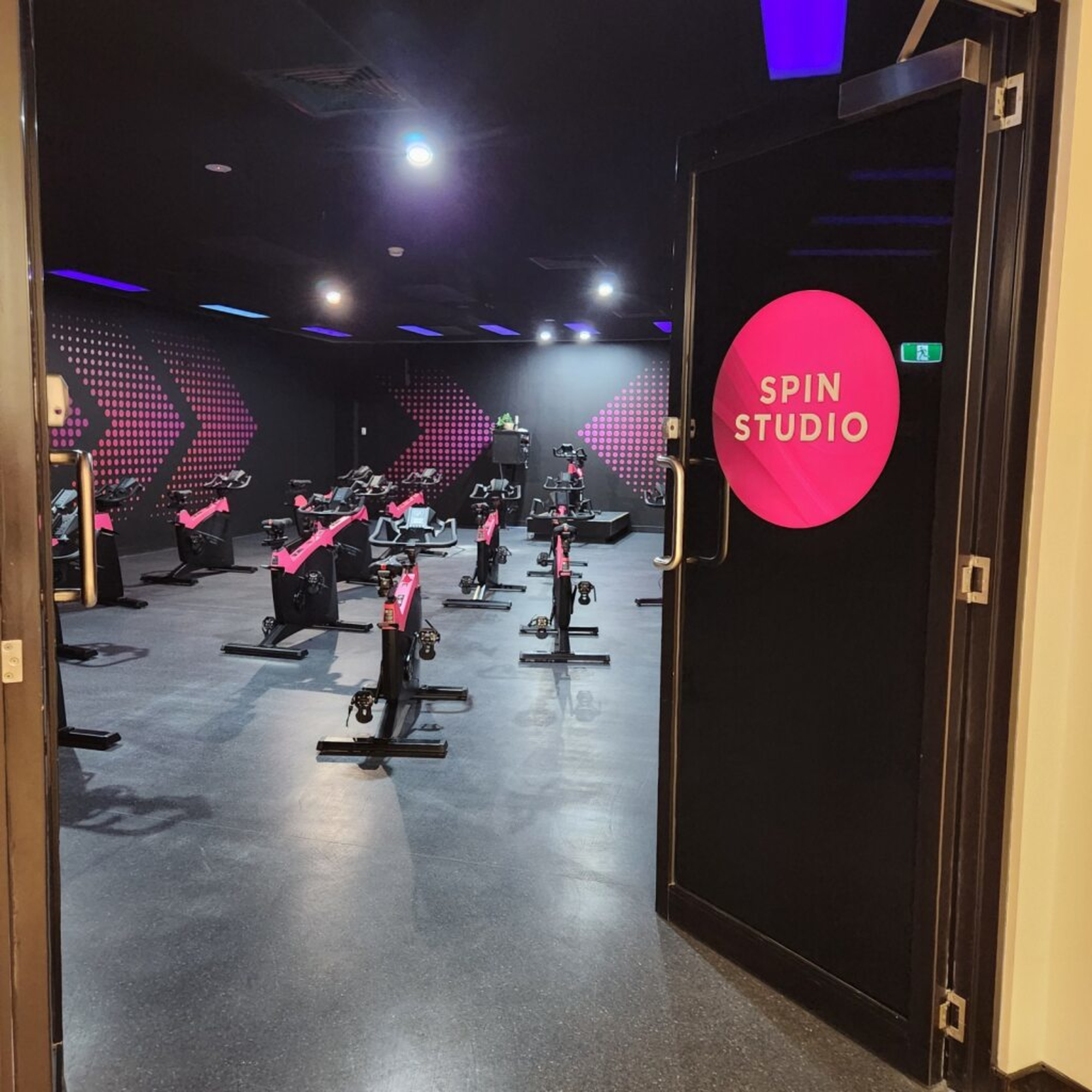 Modern indoor spin studio with rows of stationary bikes and neon pink accents.